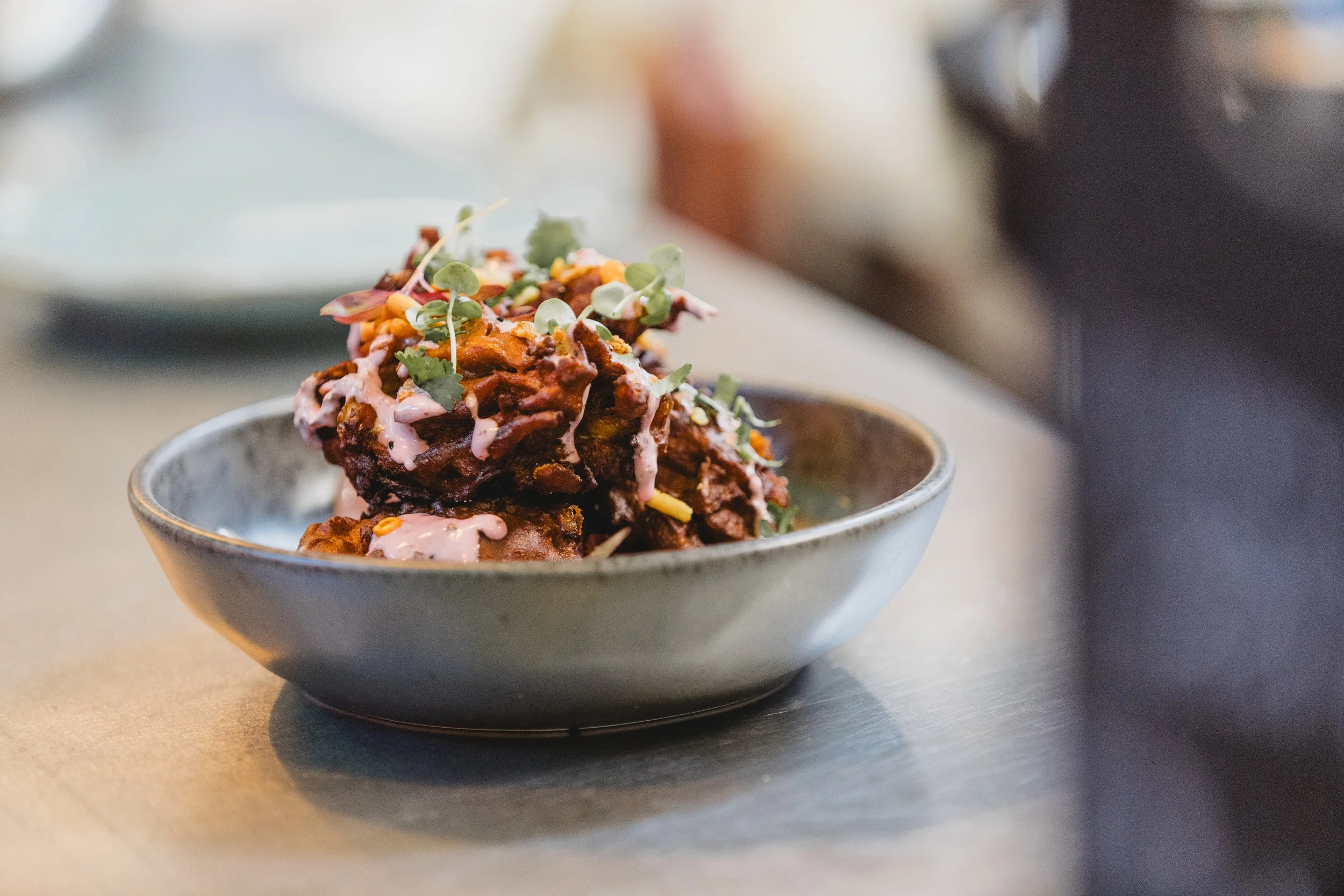 Bowl of spicy beef or chicken topped with microgreens and pink sauce on a gray table.