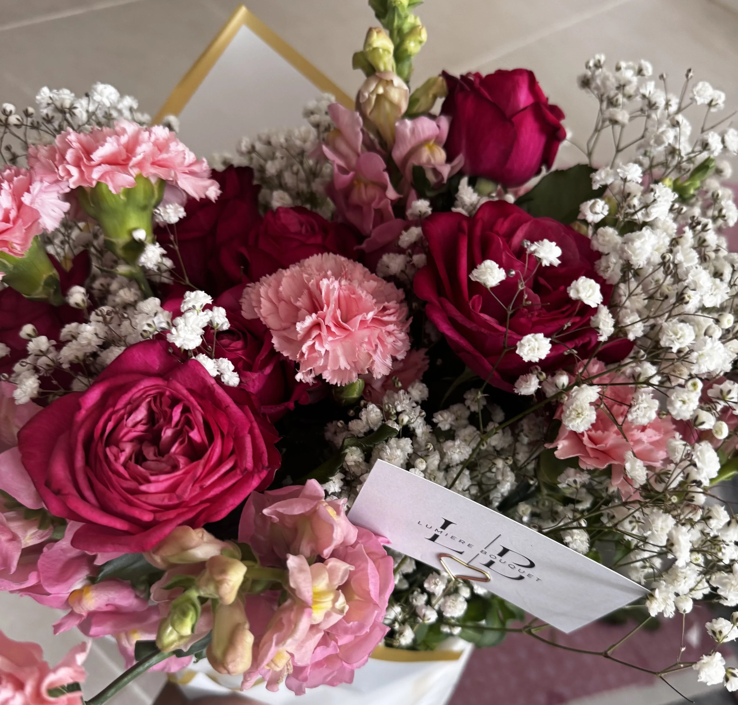 A bouquet of pink and red roses, pink and white carnations, white baby's breath flowers, and greenery with a white card attached.