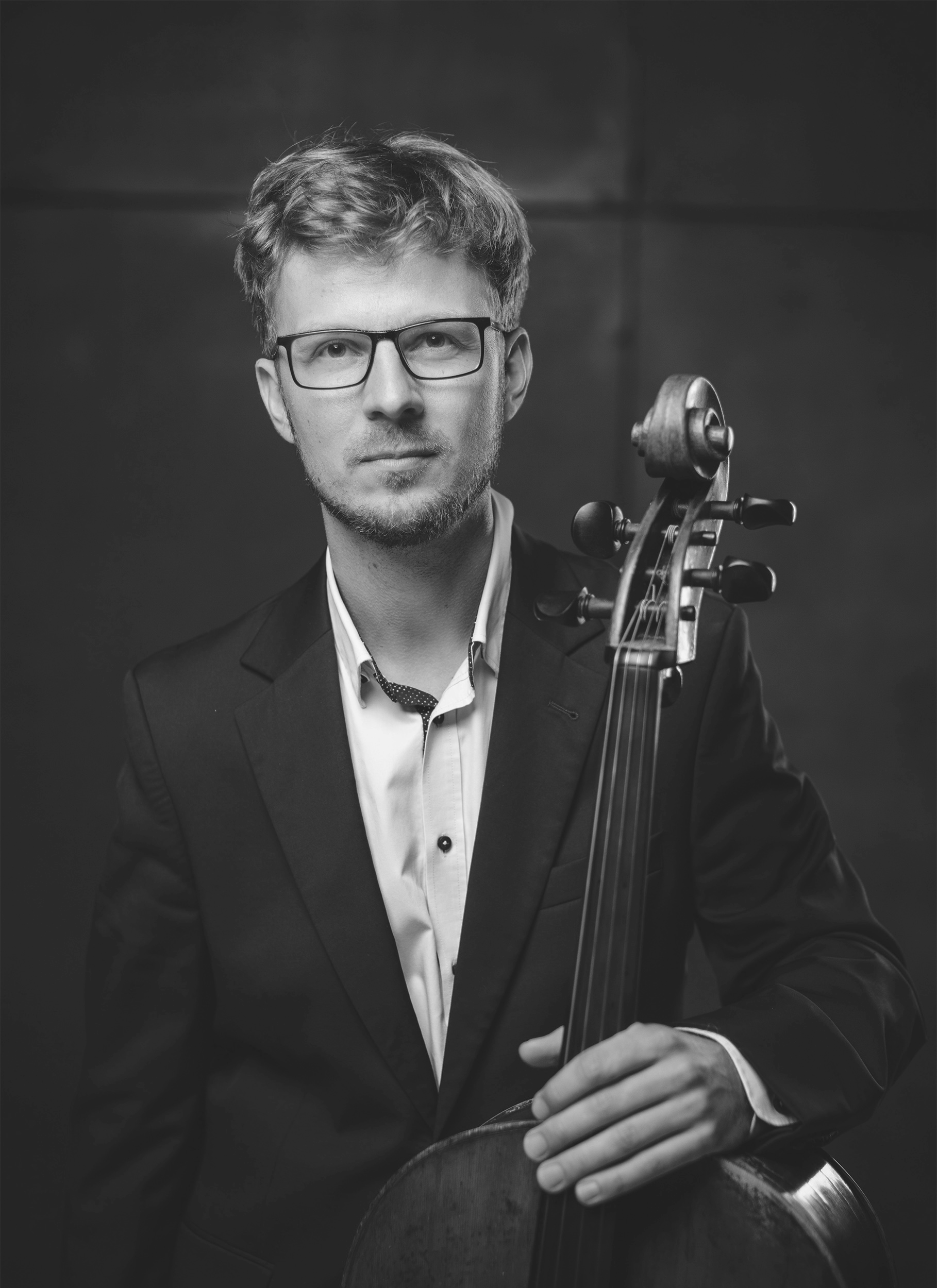 Black and white portrait of a man in a suit with glasses holding a cello.