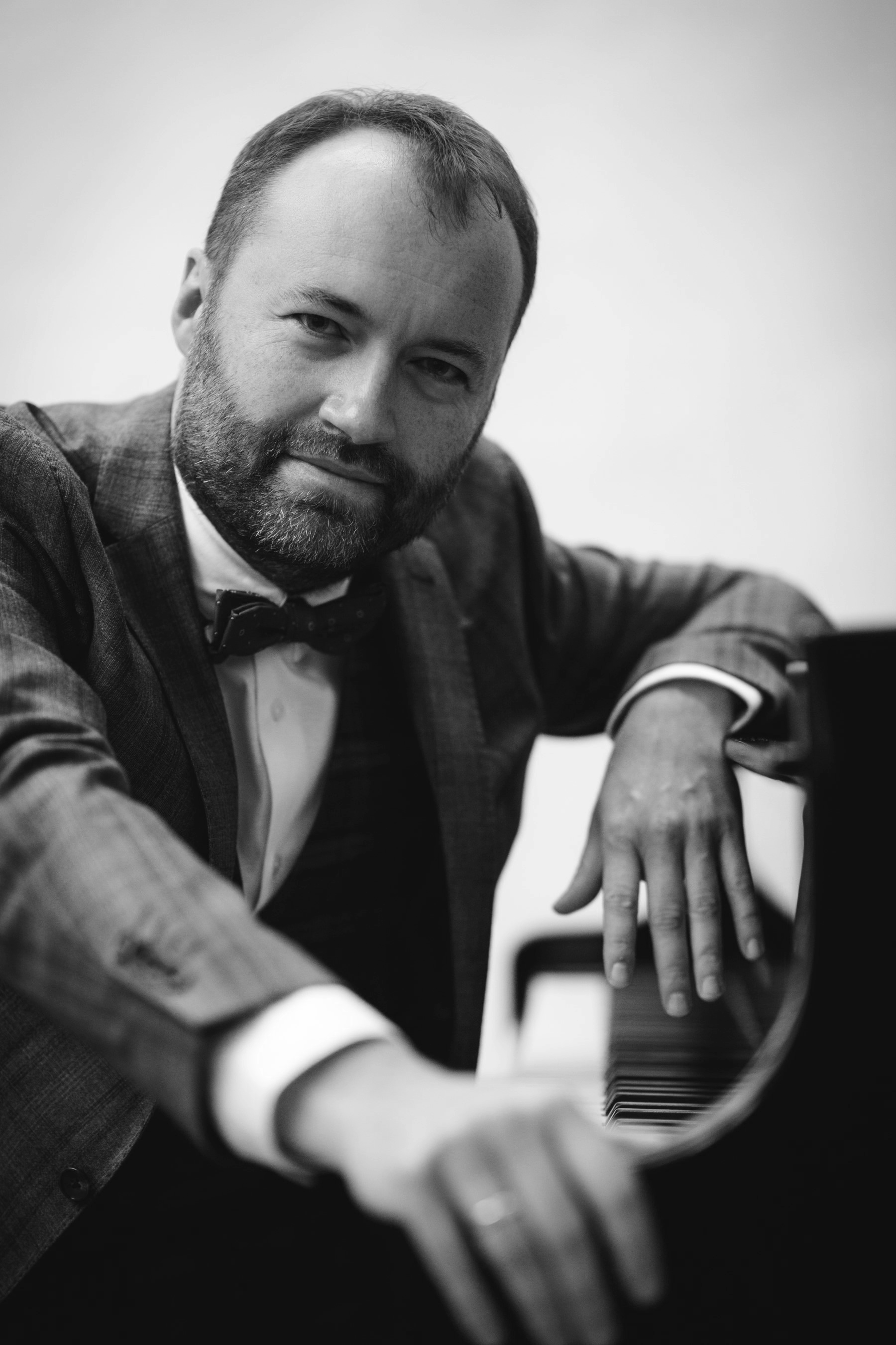Black and white photo of a man in a suit and bow tie playing a grand piano.