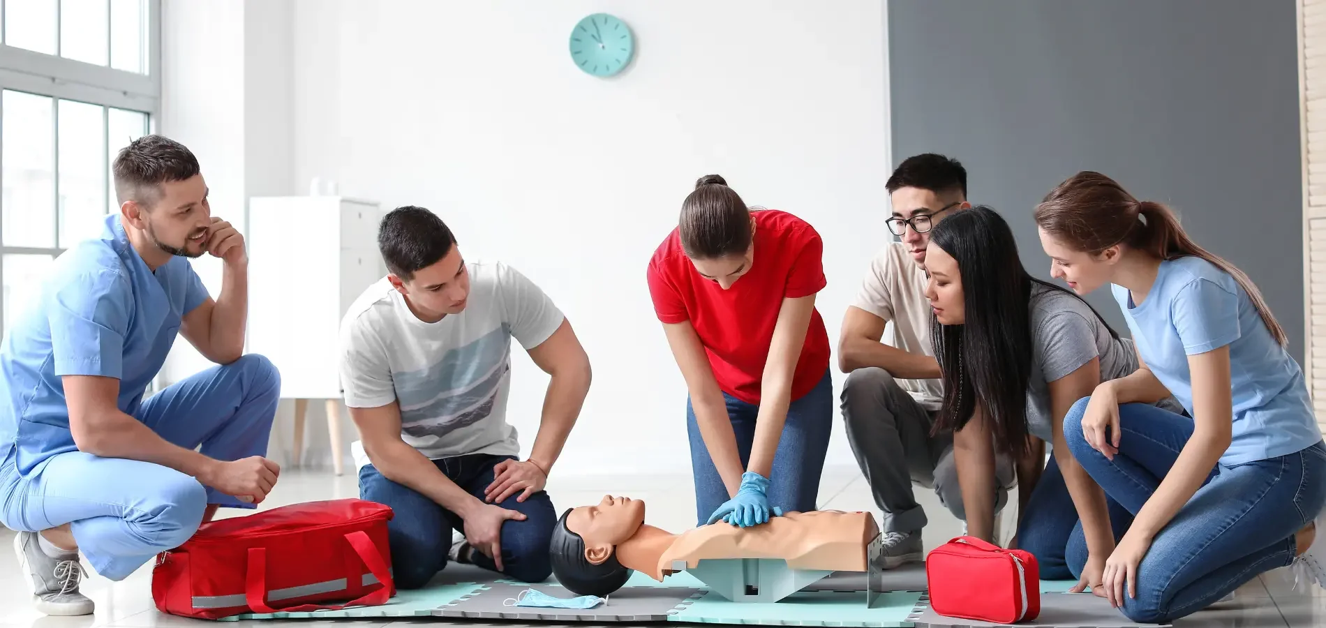 Group of people practicing CPR on a training mannequin in a classroom setting.