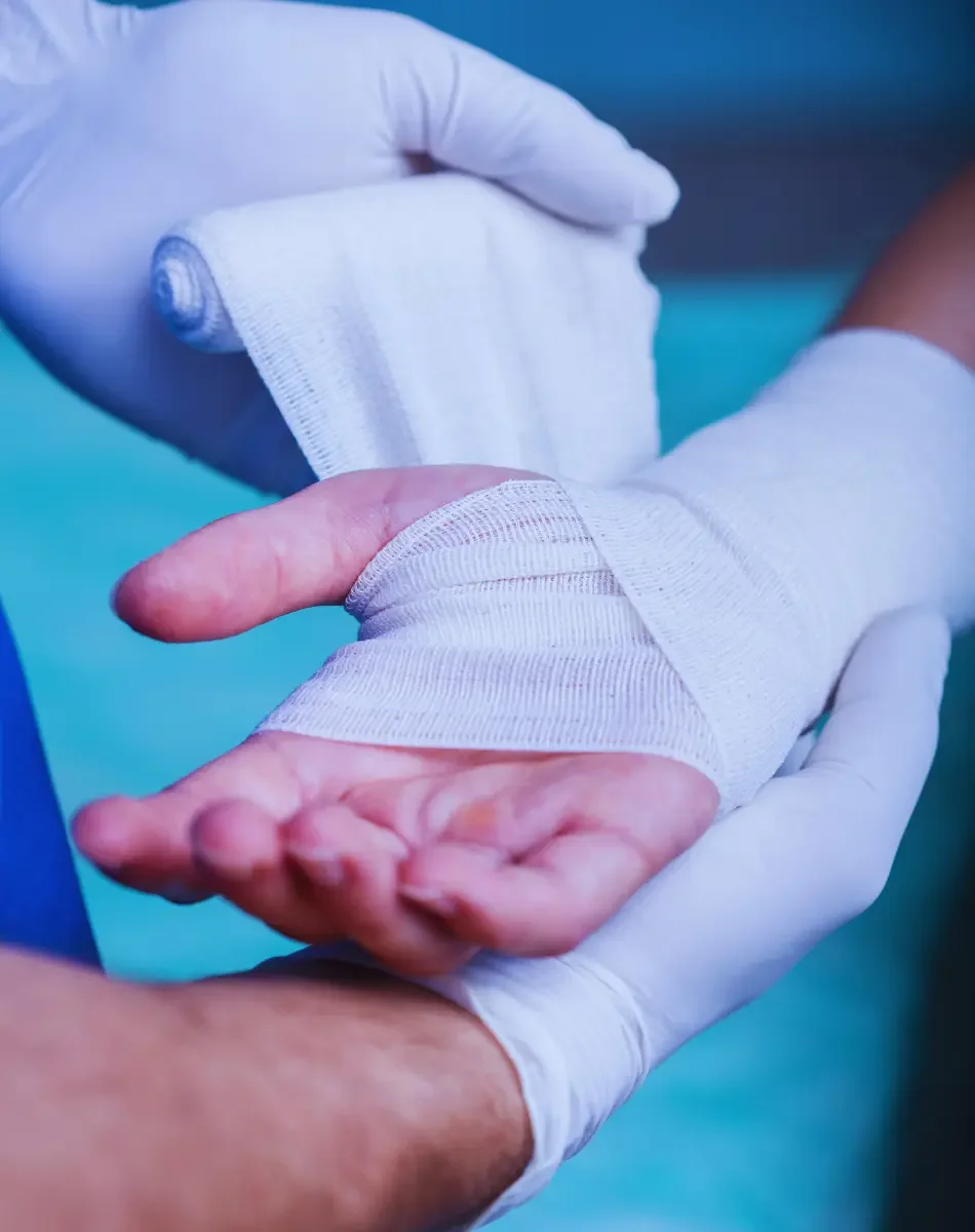 A healthcare worker with gloves wrapping a person's hand with white medical tape.