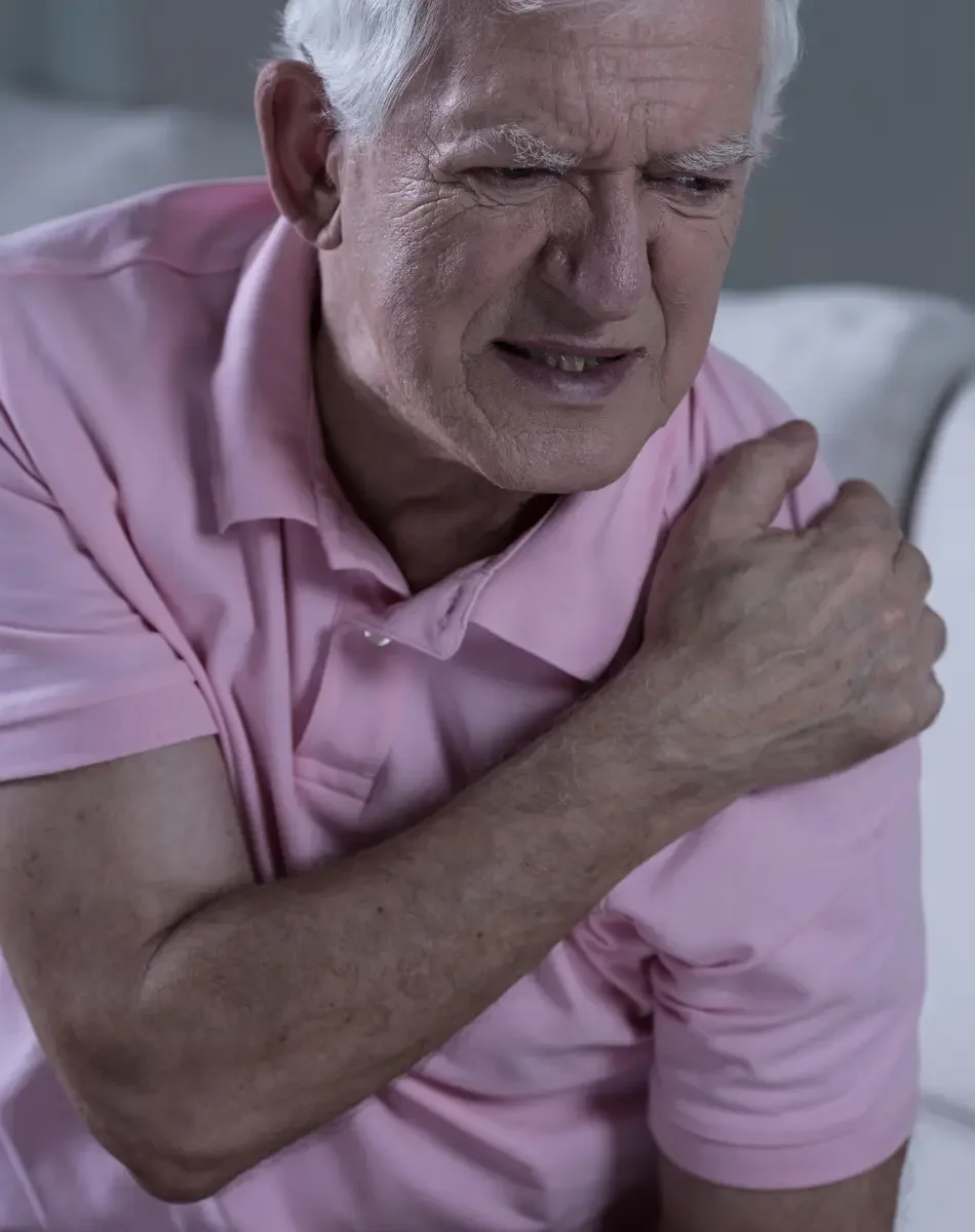 An elderly man in a pink shirt appears to be experiencing chest pain or discomfort, clutching his chest with a pained expression on his face.