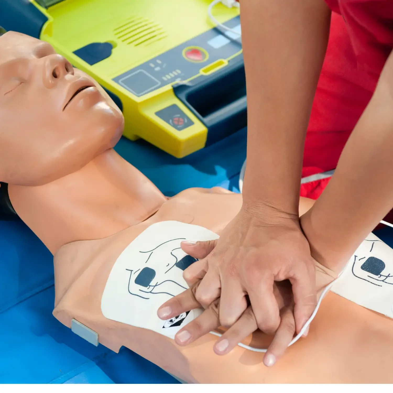 A person performing CPR on a medical training dummy, with a defibrillator nearby.