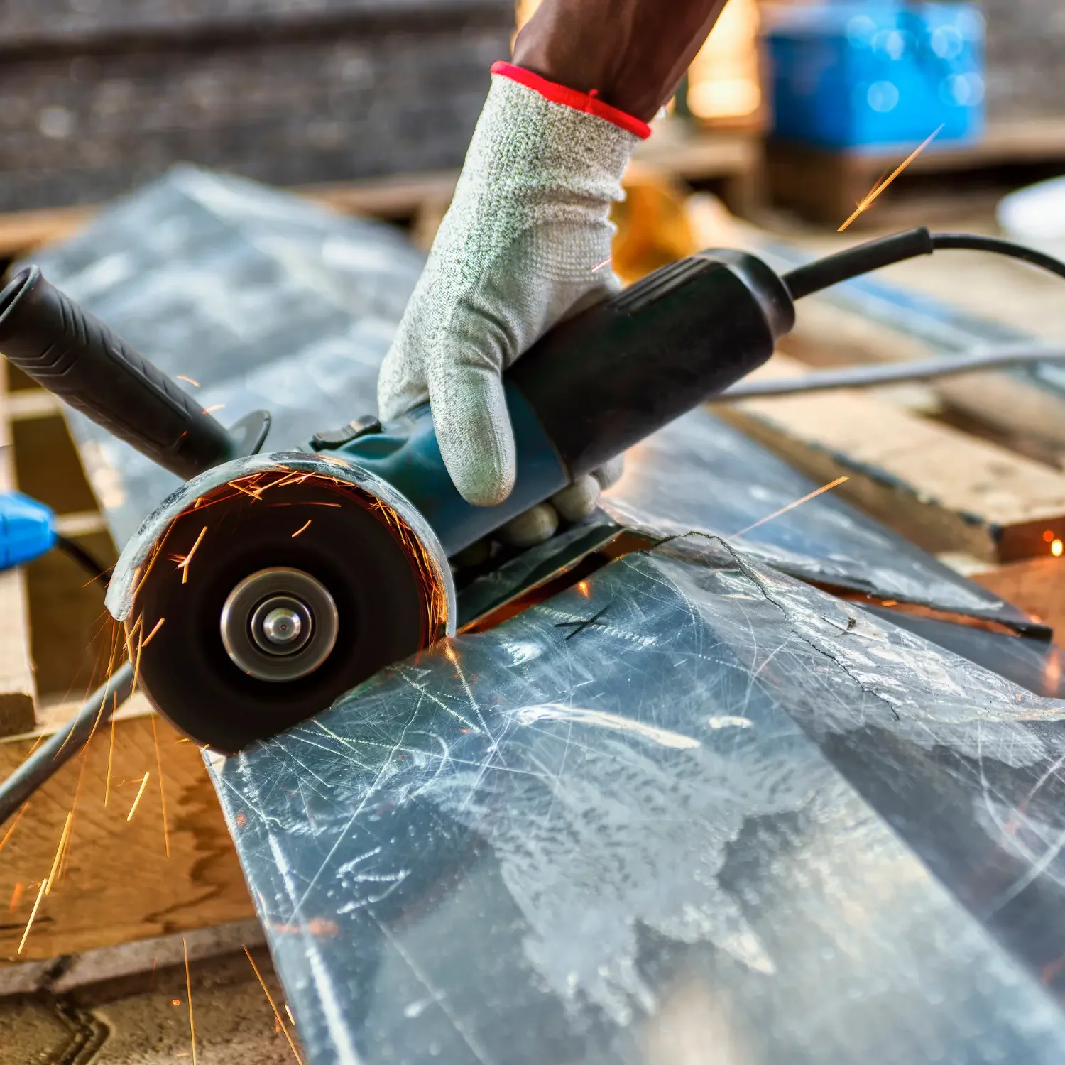 Person wearing gloves uses an angle grinder to cut metal sheet, sparks flying.