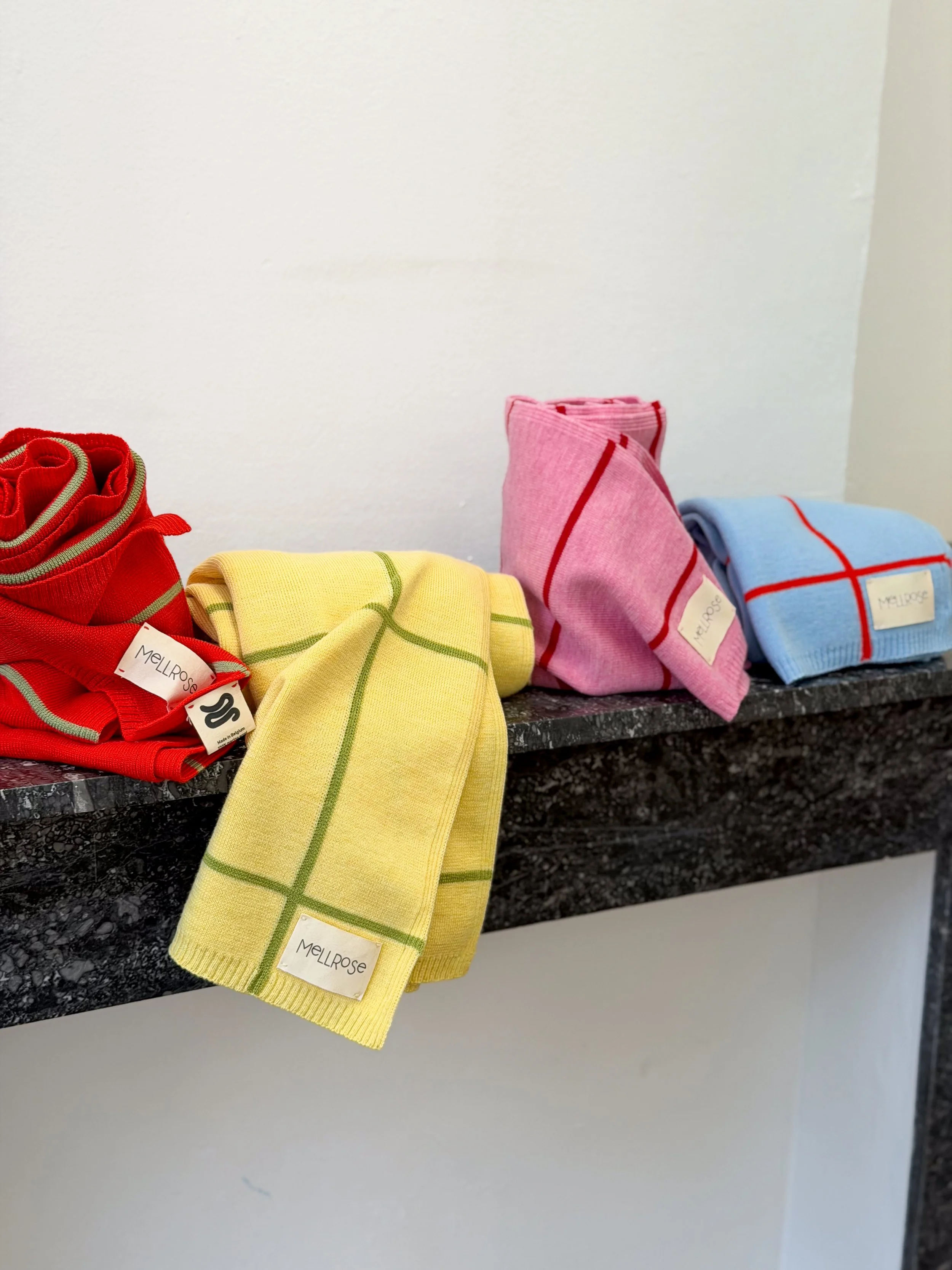 Four folded colorful merino baby blankets  with labels on a black marble ledge.