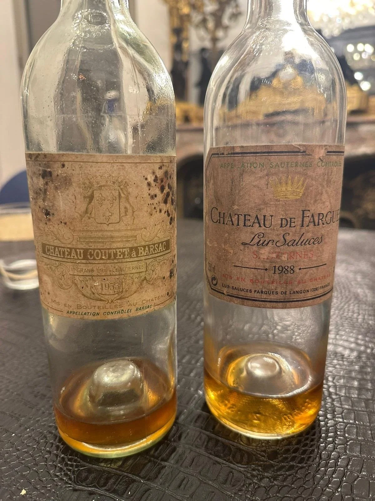 Two partially filled vintage glass bottles of wine with old labels, set on a textured surface with a blurred background.