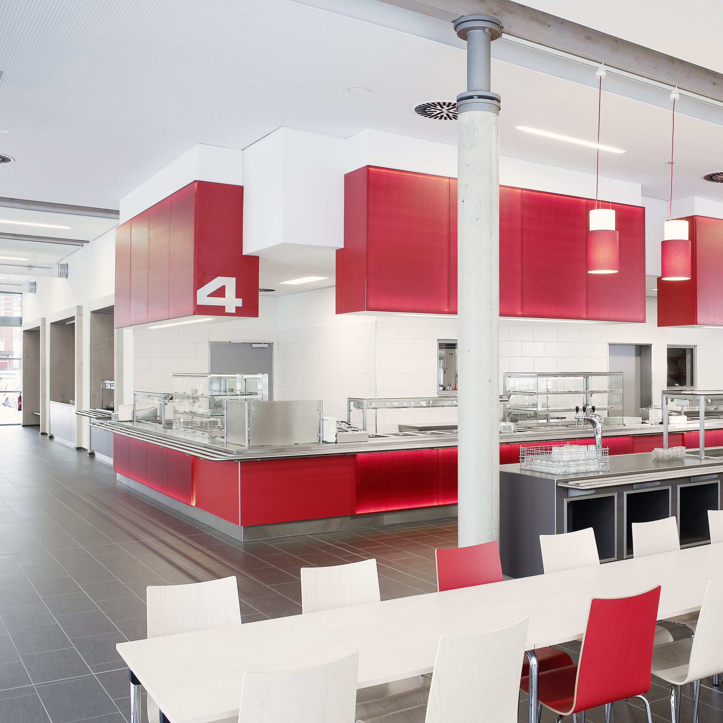 In diesem Bild ist eine moderne, leere Cafeteria mit rot-weißen Farbthemen, offenem Essbereich und Servicetheke zu sehen.