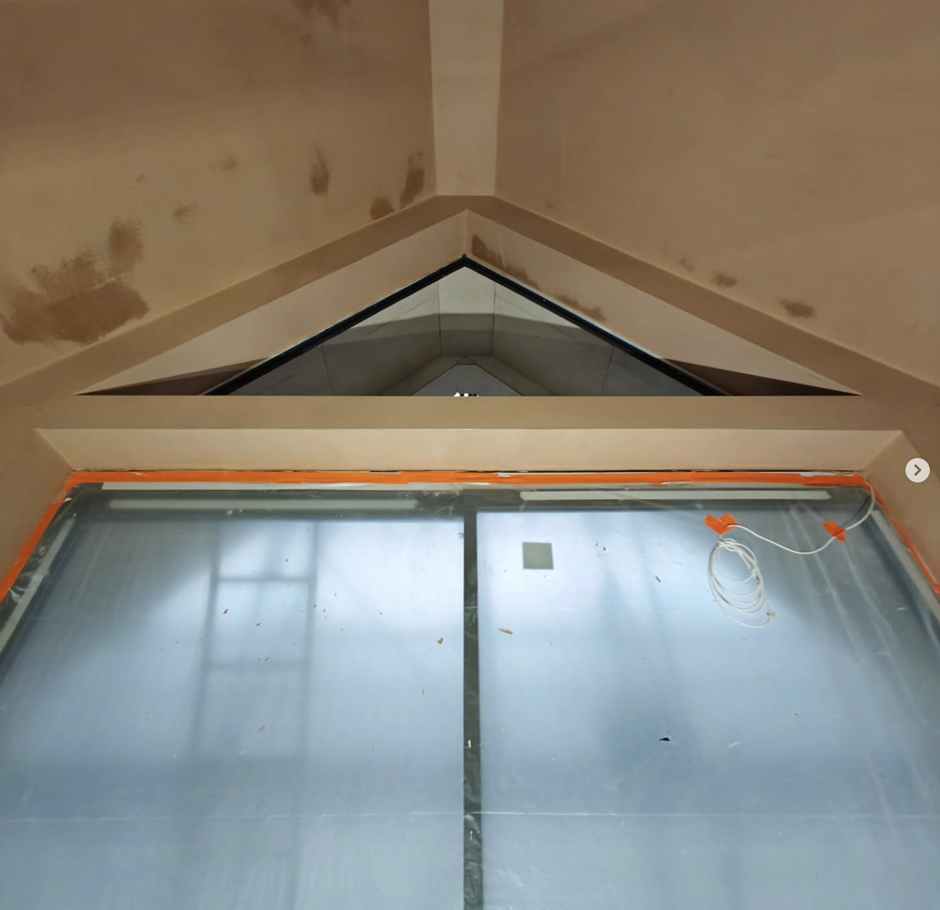 Interior view of a building under construction, showing a pyramid-shaped window and a ceiling with exposed plastered drywall and electrical wiring.