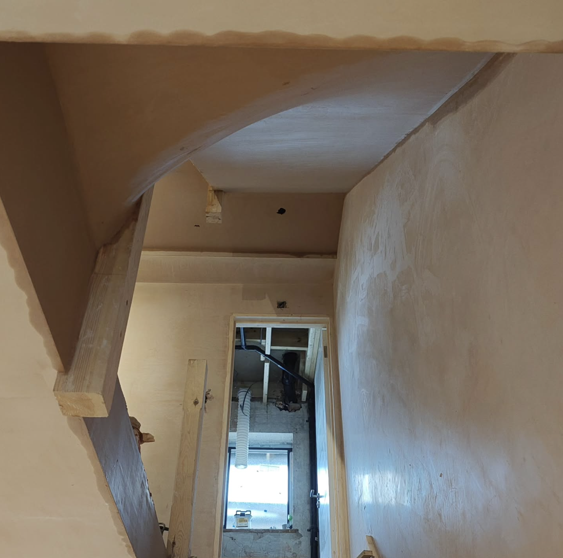 Interior of a house under construction with wooden framing and drywall installation and plastering in progress.
