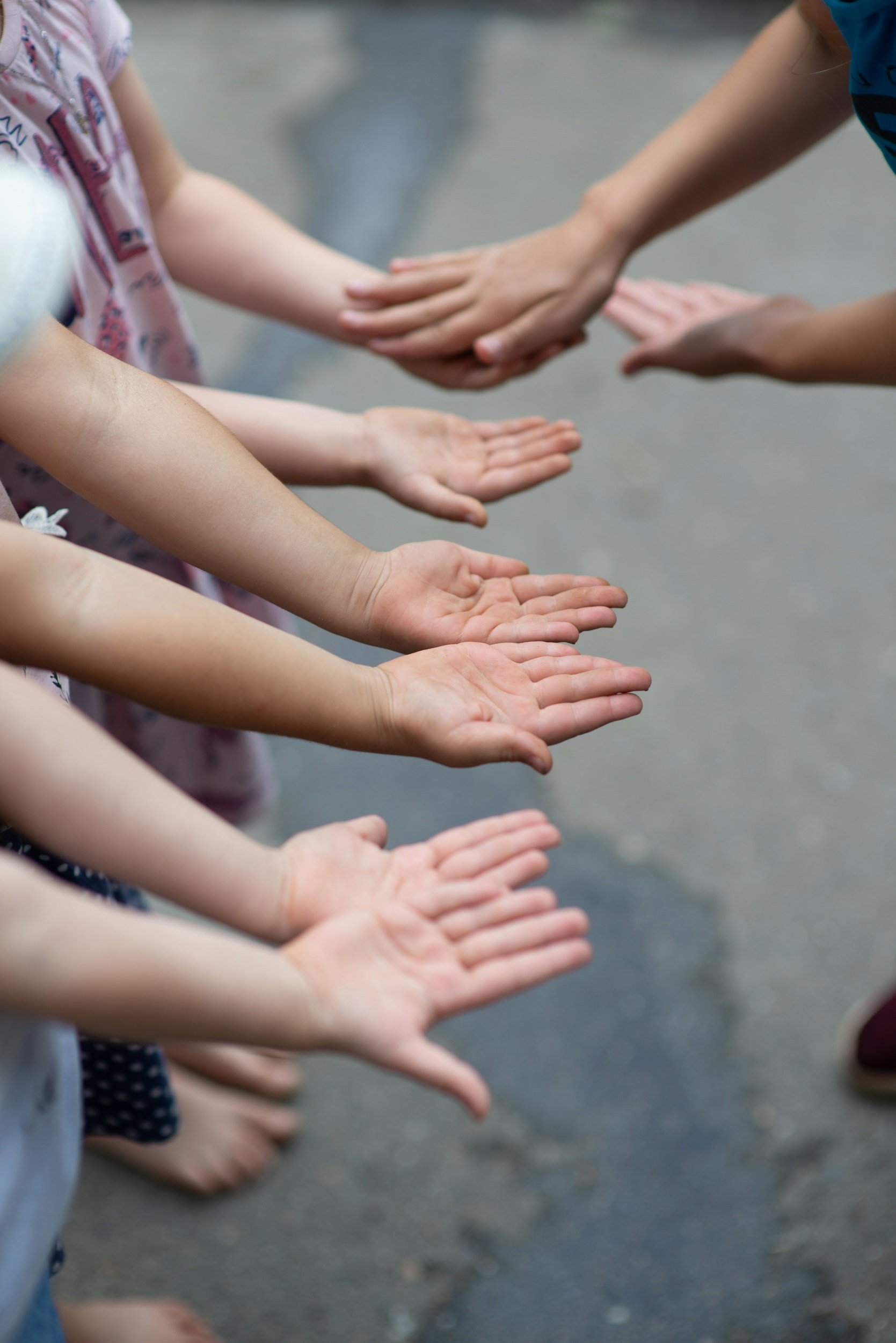 Children and adult reaching out with hands extended and palms open, standing on asphalt surface.