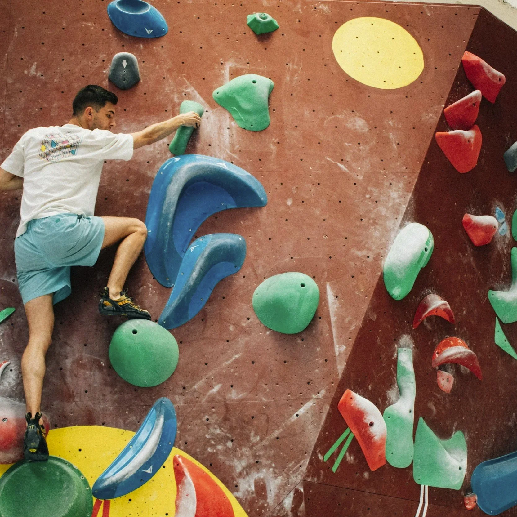 Jemand klettert an einer Wand mit Klettergriffen in verschiedenen Farben bei einem Indoor-Kletterpark.