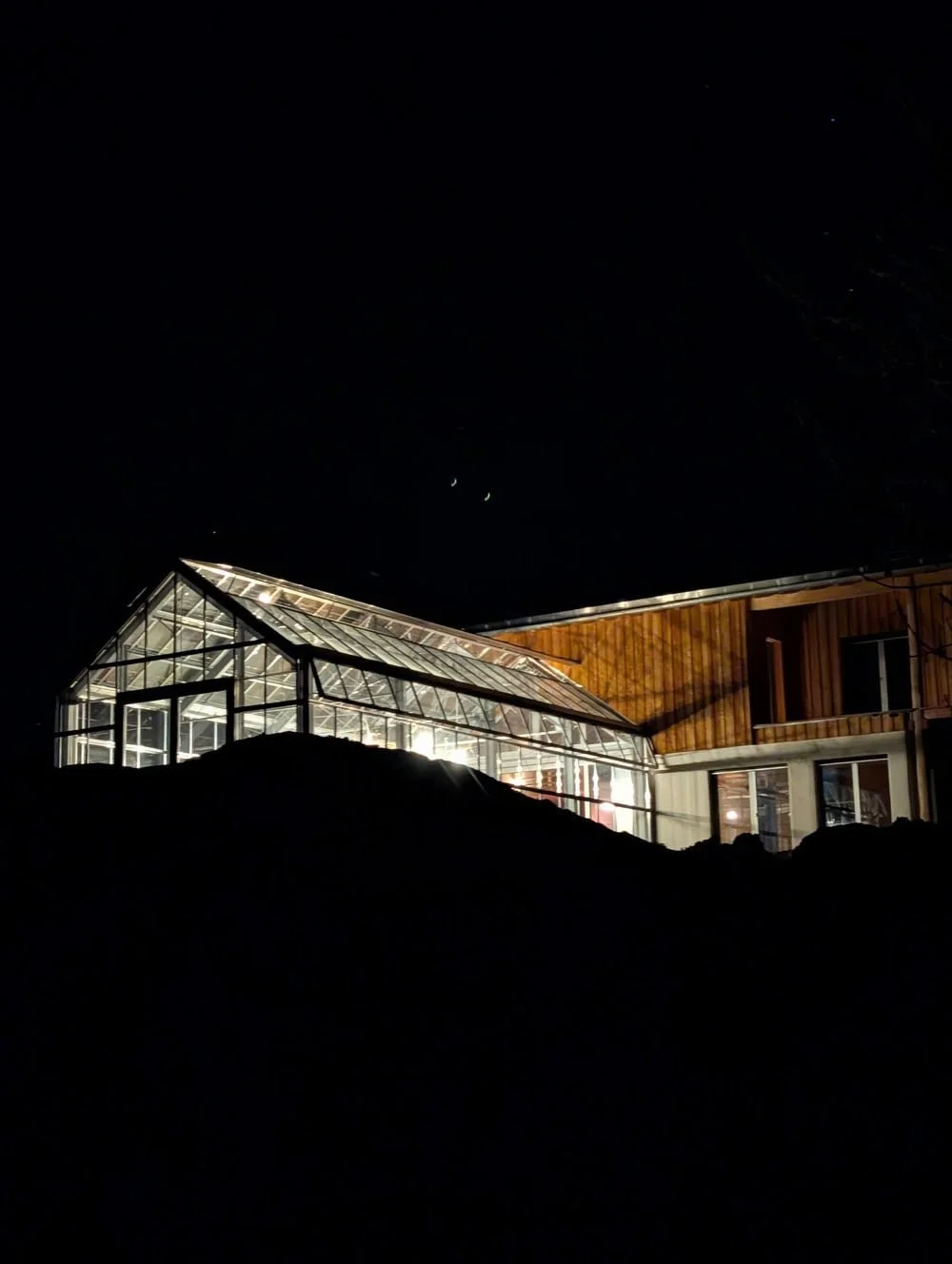 Ein Haus mit einem beleuchteten Wintergarten bei Nacht, umgeben von Dunkelheit.