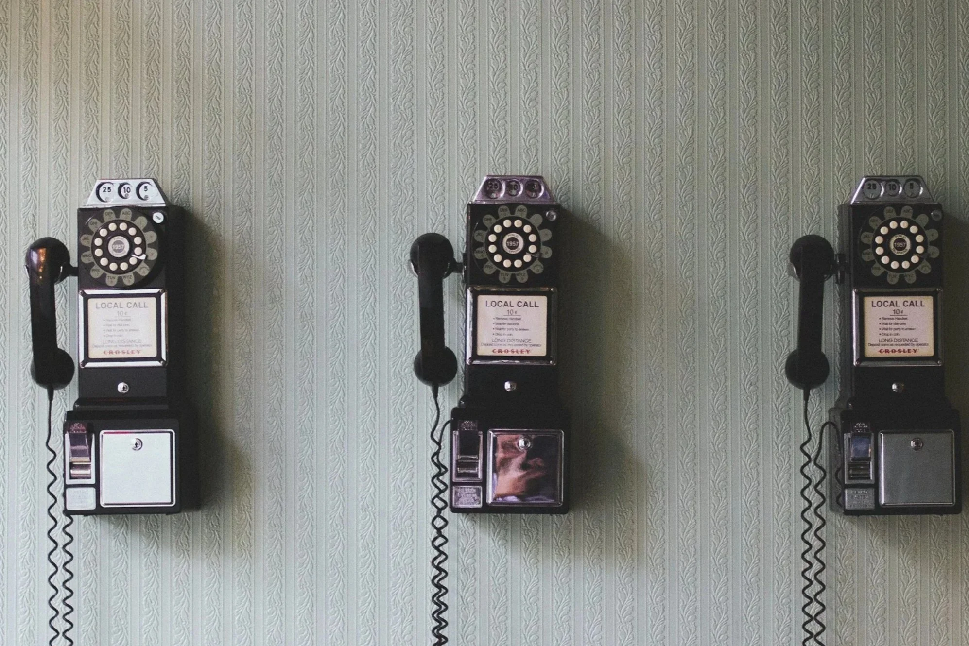 Drei alte Münzfernsprecher an einer Wand mit grünem Muster