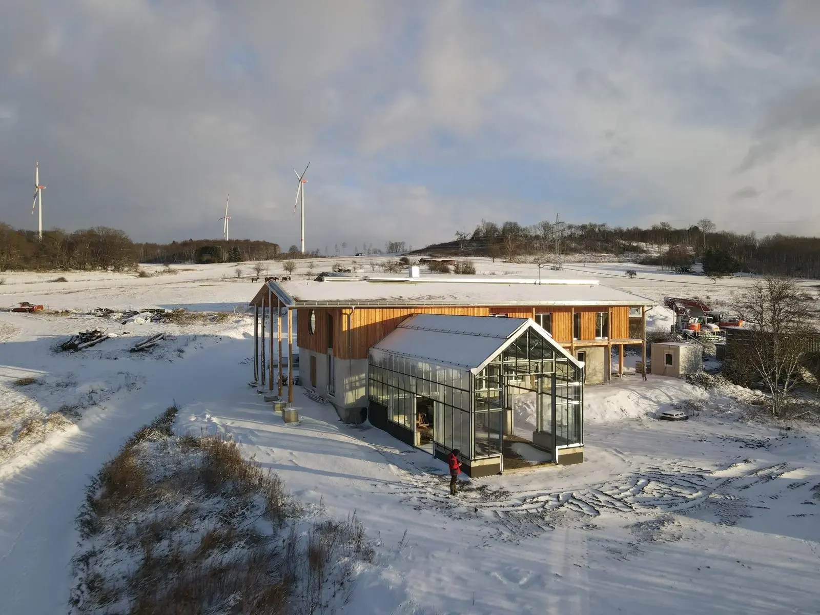 Ein Gebäude im Bau, umgeben von verschneiter Landschaft, mit Windkraftanlagen im Hintergrund und einem klaren Himmel.