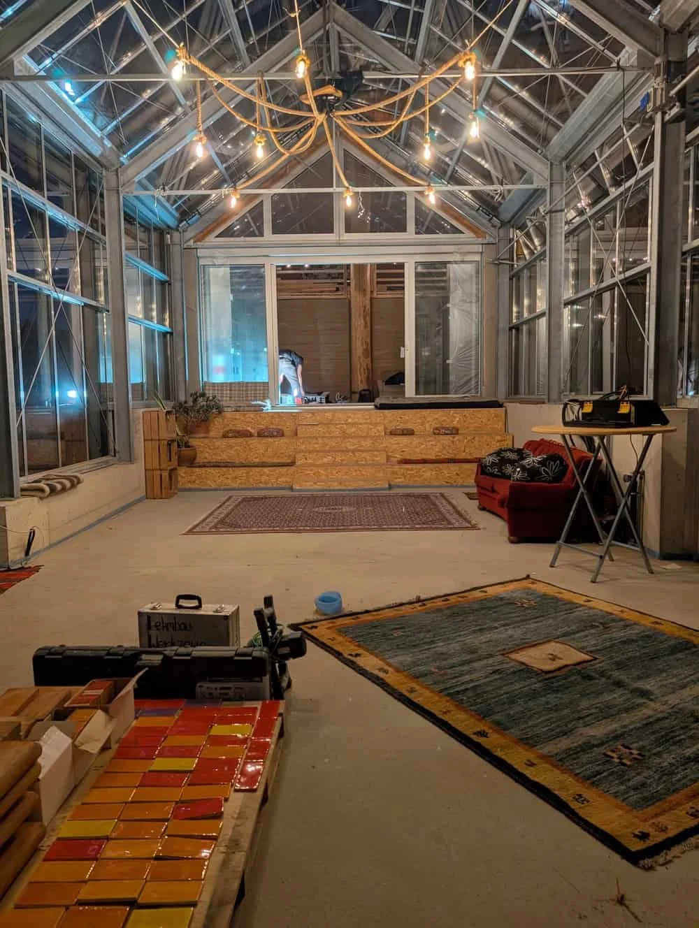 Innenansicht eines Konferenzraums mit Glaswänden, Holzboden, Teppichen und rustikalen Lampen an der Decke, umfangreiche Beleuchtung und moderne Einrichtung.