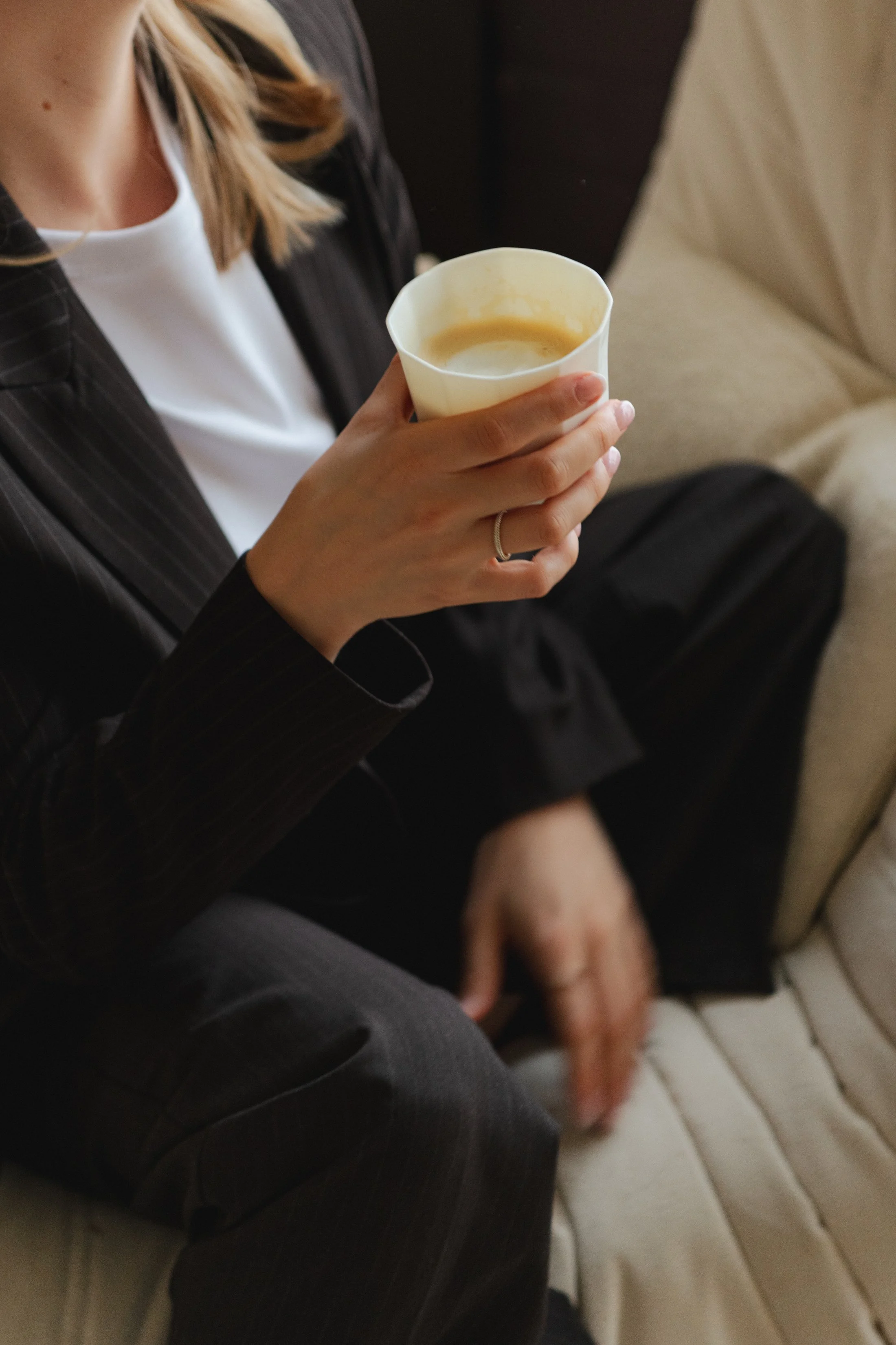 Een persoon die een kopje met koffie vasthoudt, zittend op een bank.