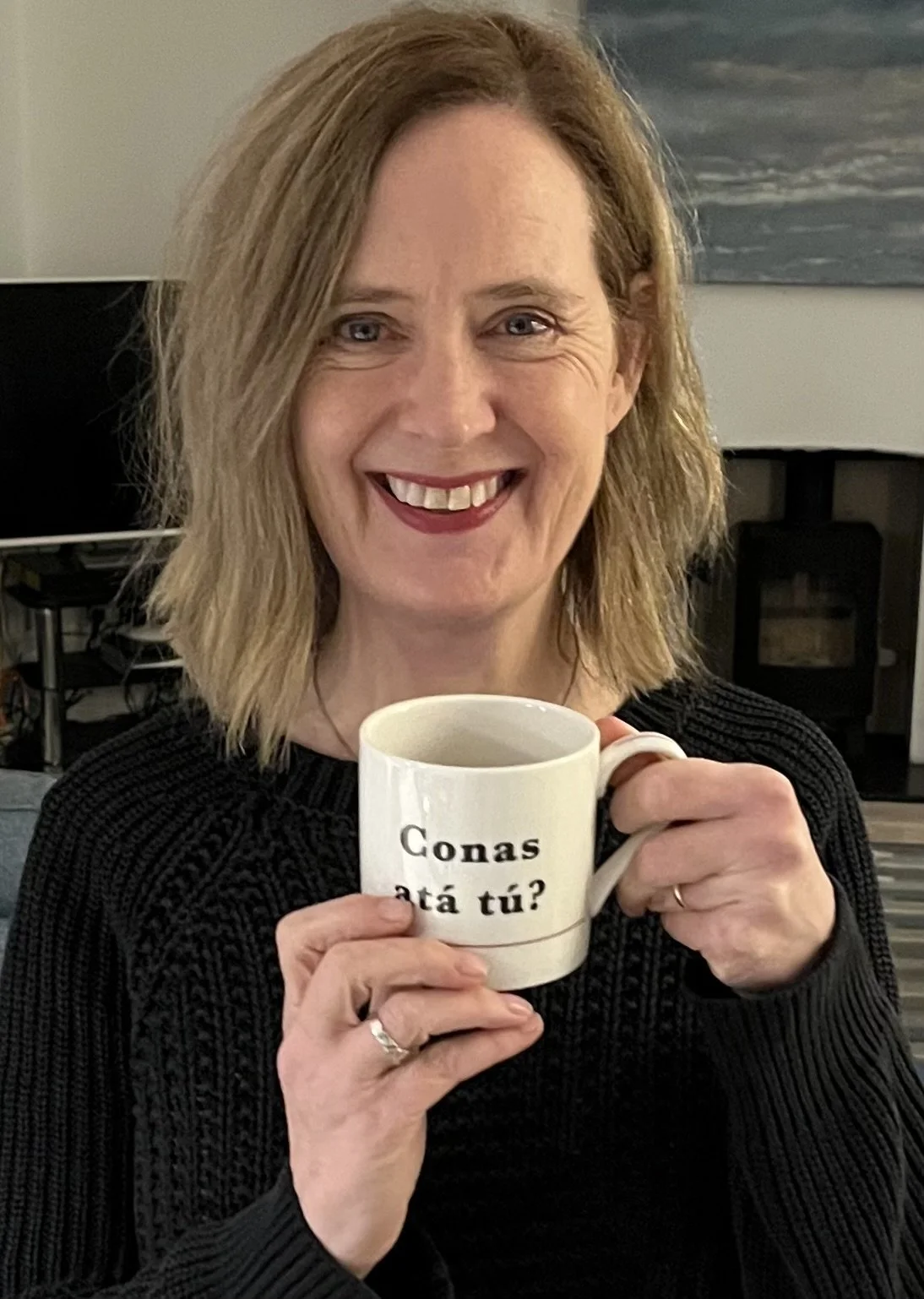 Smiling woman holding a mug which says Conas ata tu, which is Irish for how are you?