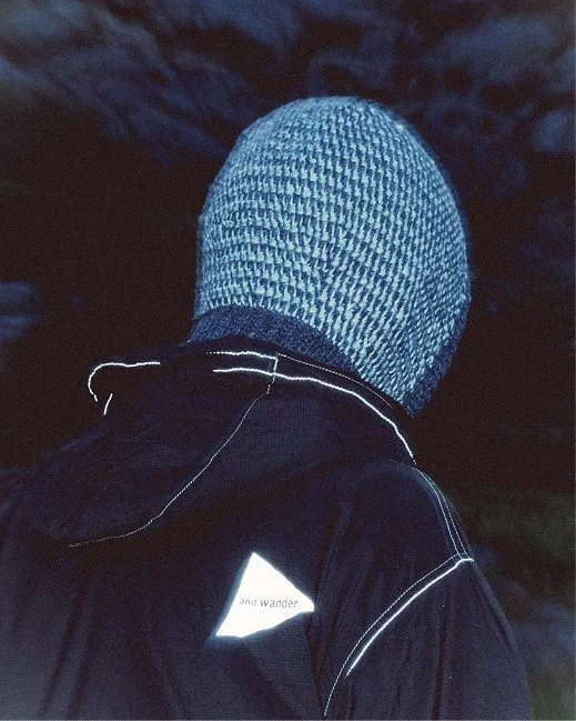 A person wearing a wool knit Clara Knitwear Brenna Hood and a black jacket with reflective stitching.