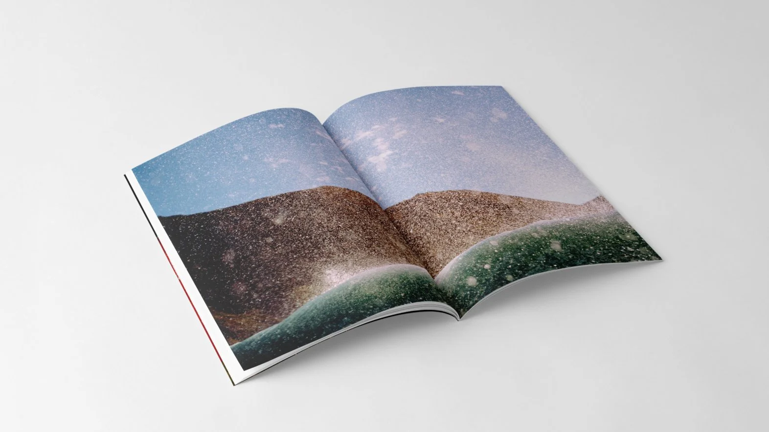 An open magazine displaying a landscape photo of mountains and a body of water in the foreground, with a wave splashing overhead.