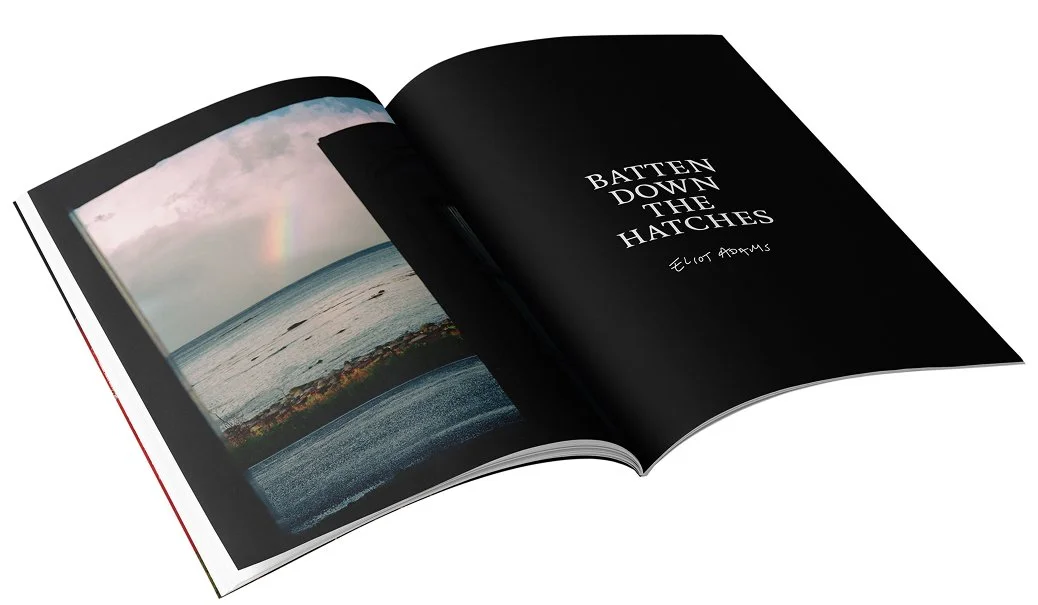 An open zine showing a picture of a rainbow over the ocean on the left page and the title 'BATTEN DOWN THE HATCHES' with the author's name Eliot Adams on the right page.