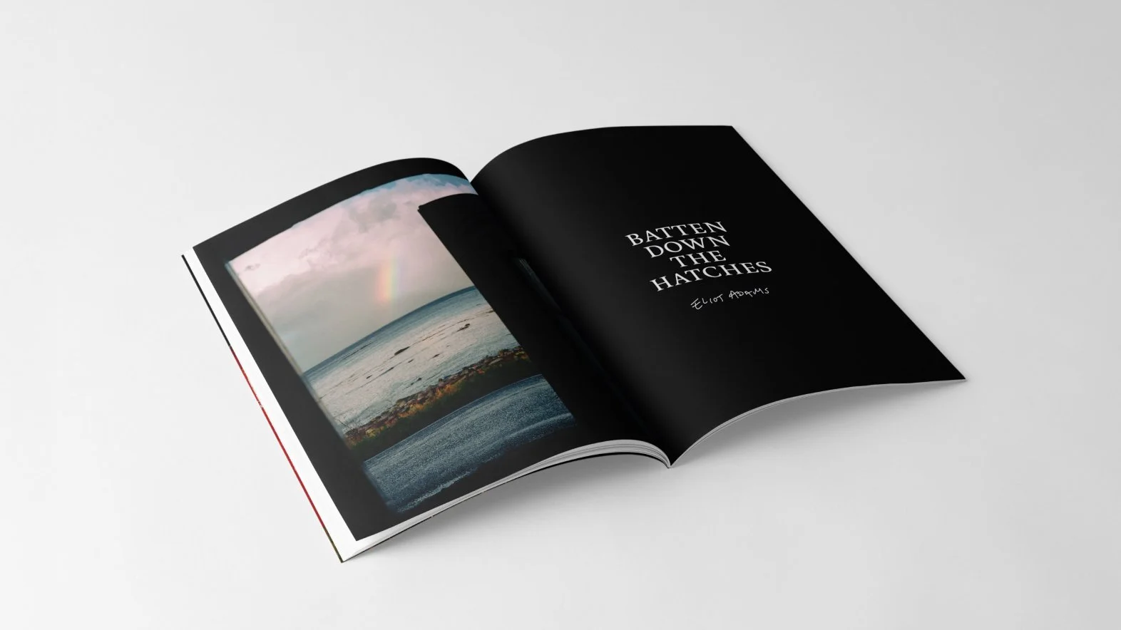 Open magazine displaying a photograph of the ocean with a rainbow, and a black page with white text that reads 'BATTEN DOWN THE HATCHES' and additional smaller text.