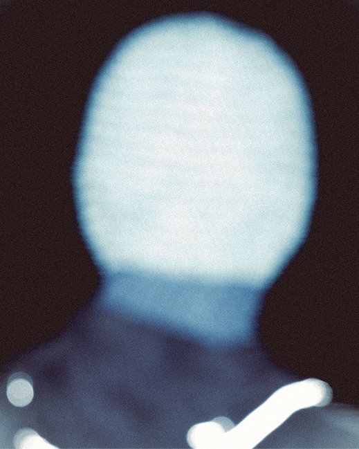 Out-of-focus close-up of a person's head, wearing a Clara Knitwear Brenna Hood, against a dark background.