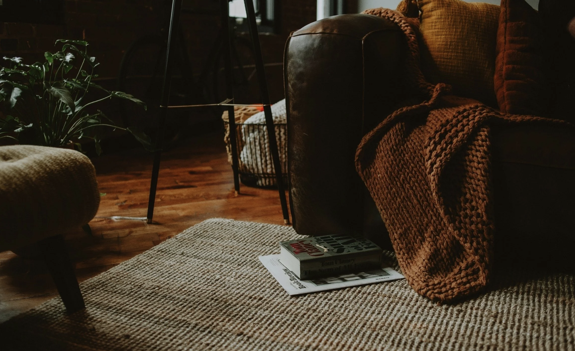 A dimly lit living space featuring a dark leather couch, a heavy blanket, and a book abandoned on the rug, representing the hidden exhaustion and private collapse of entrepreneurs experiencing shadow burnout in Pinehurst and Moore County, NC.