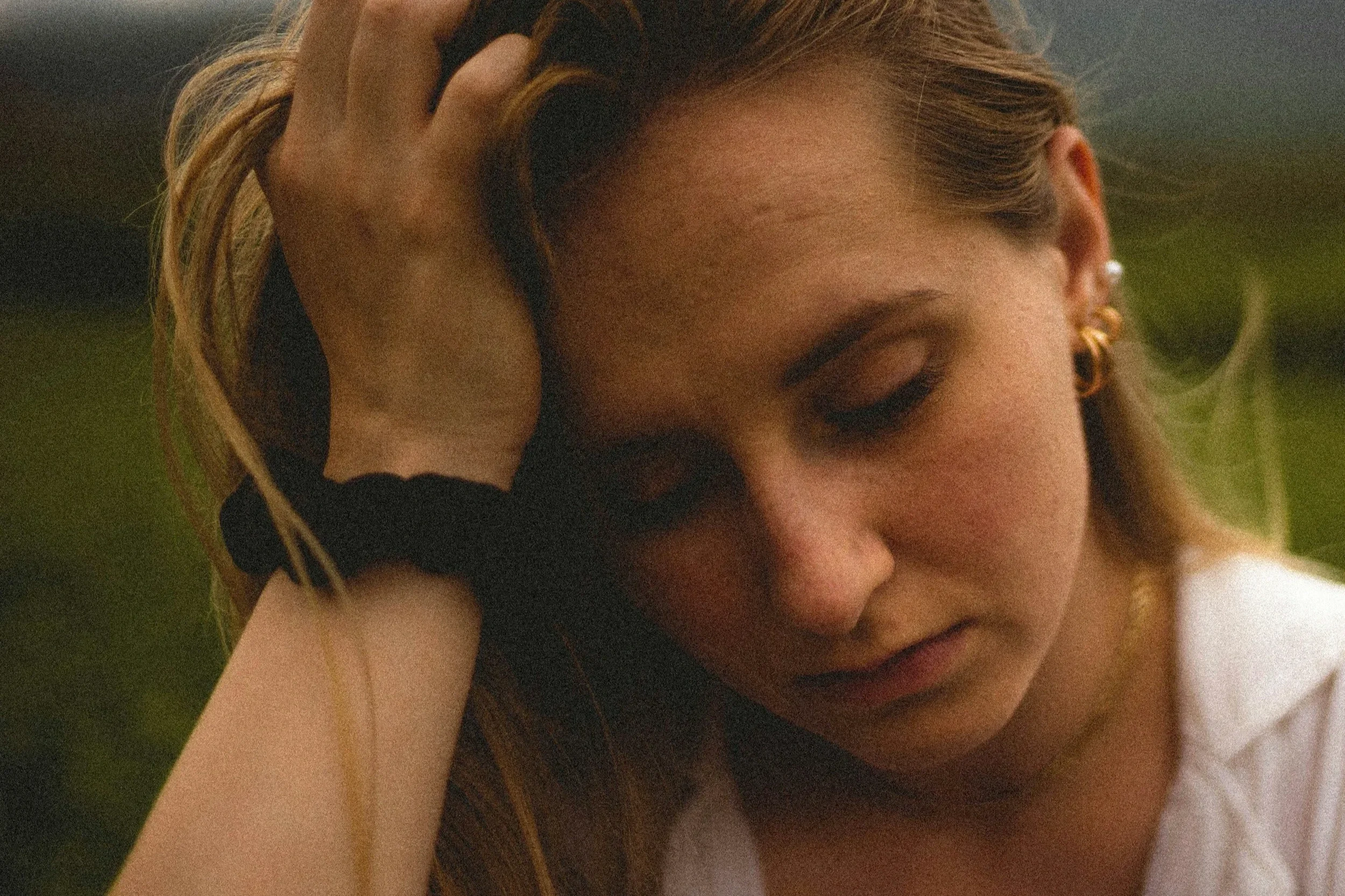 A reflective woman resting her hand in her hair, representing emotional exhaustion and the hidden impact of trauma on mental health.