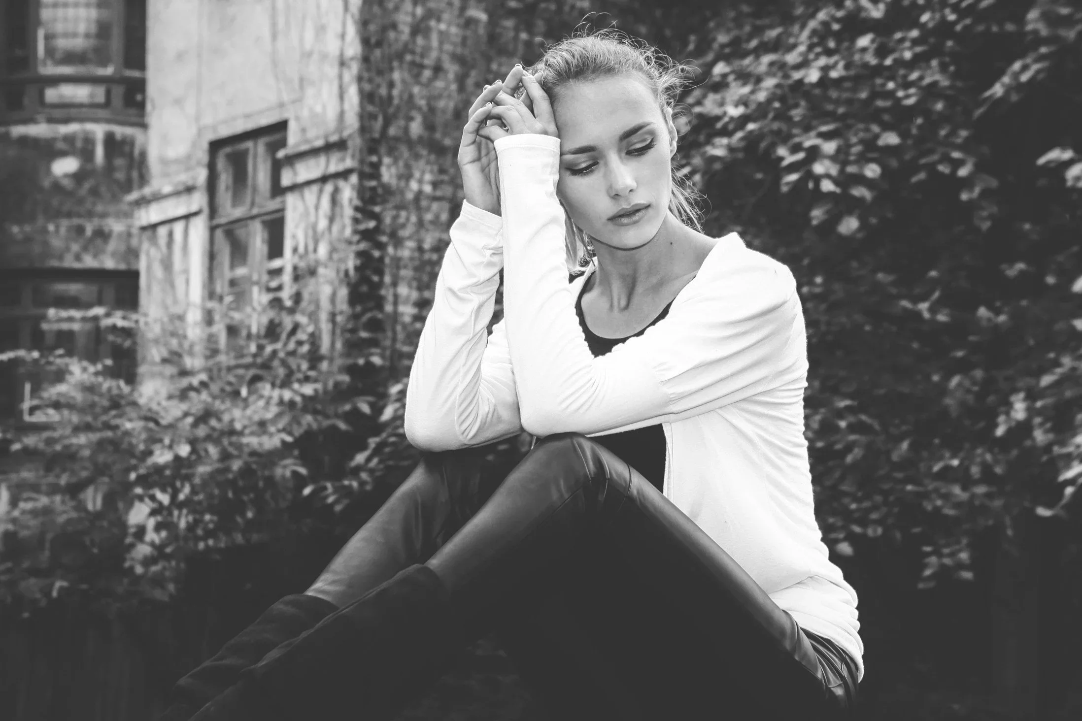 Black and white photo of a woman looking exhausted and overwhelmed, resting her head against her hands, representing trauma burnout and emotional fatigue.