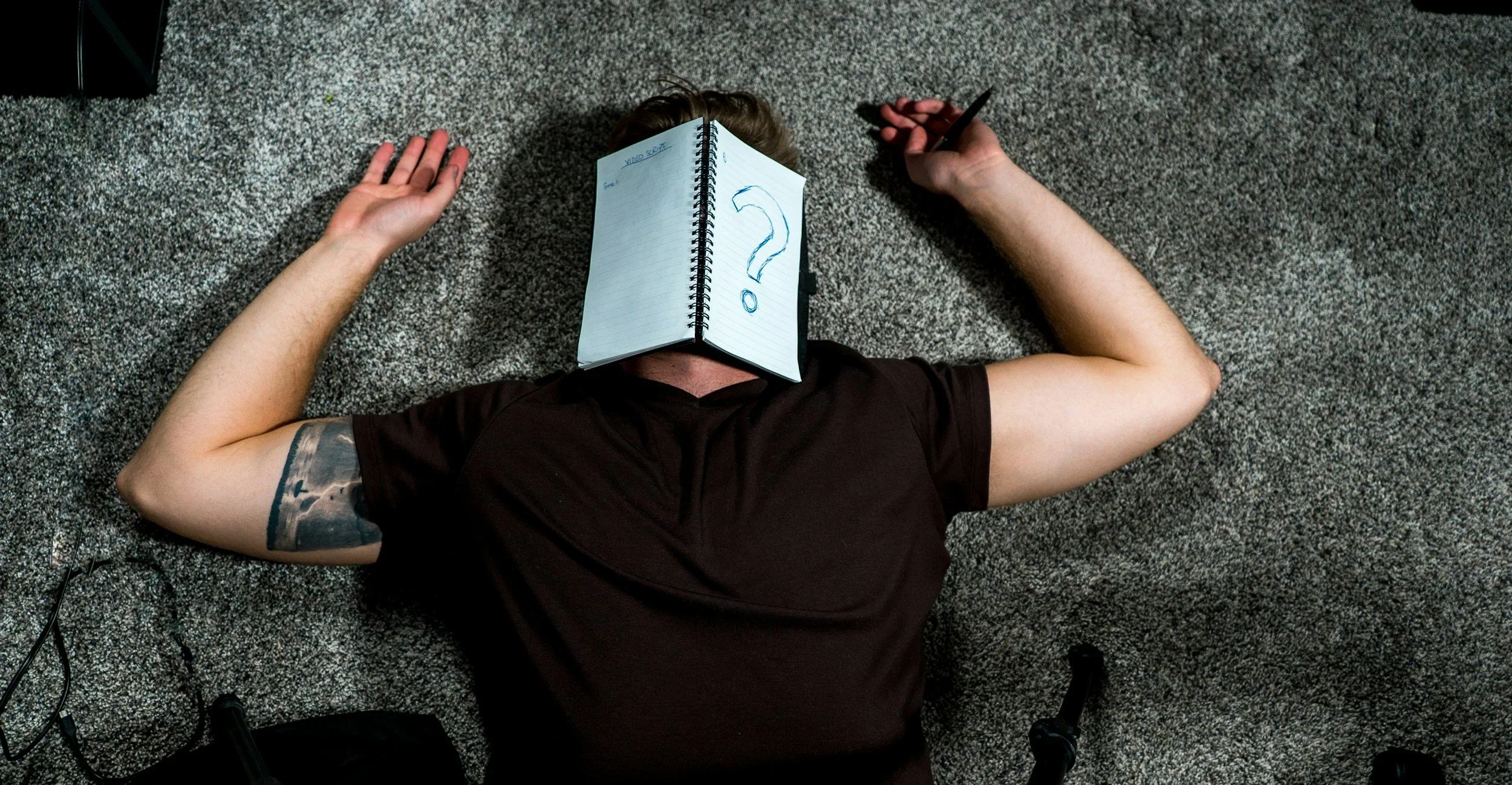 An exhausted person lying face-up on a carpeted floor, with their face covered by a notebook showing a large question mark, symbolizing the confusion and overwhelm of high-achiever burnout or narcissistic abuse recovery.