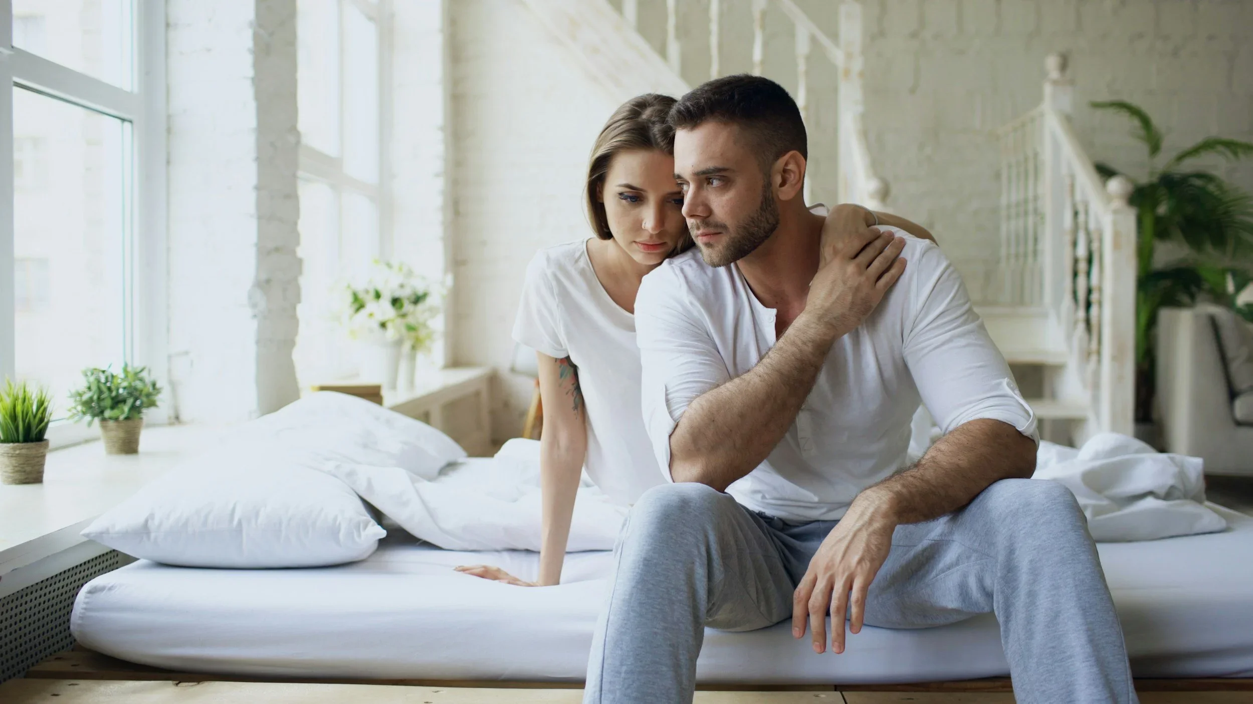 A distressed couple sitting on a bed, representing emotional disconnection and relationship struggles. Trauma therapist Mariah Zur offers specialized marriage therapy intensives to help couples heal from infidelity and rebuild trust.