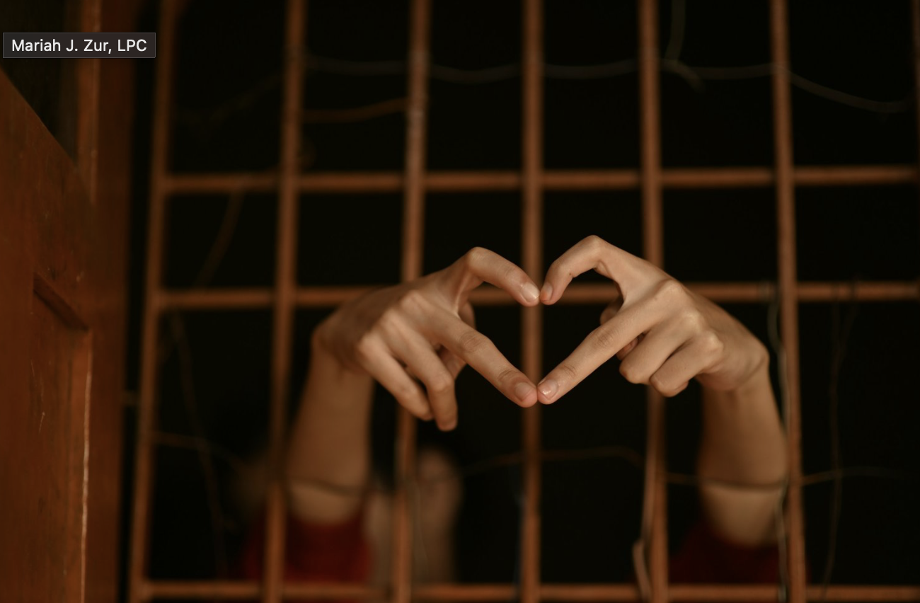 Hands forming a heart shape through rusty metal bars, symbolizing the feeling of being trapped in a trauma bond.