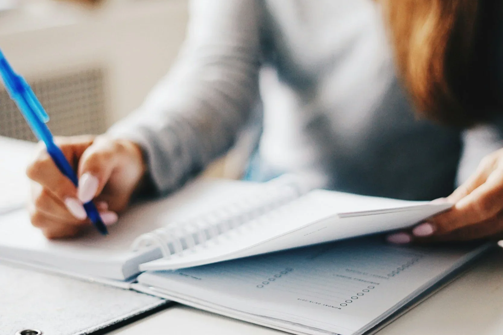 A close-up of a woman's hands writing in a notebook with a blue pen. PA trauma therapist Mariah Zur often recommends journaling to help clients process their feelings and heal from confusing relationships.