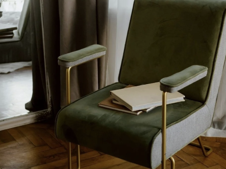 A green velvet armchair with books resting on the seat, symbolizing a safe, dedicated space for deep identity work and nervous system regulation offered through trauma therapy intensives by Mariah J. Zur in Raleigh, NC.