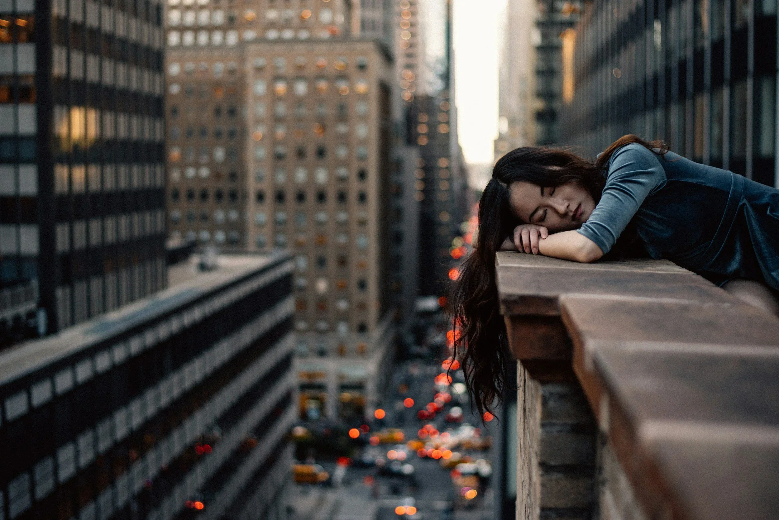 A woman rests precariously on a high-rise ledge overlooking a city, representing the emotional edge of complex trauma (CPTSD) and the need for urgent trauma therapy intensives in PA with Mariah J. Zur.