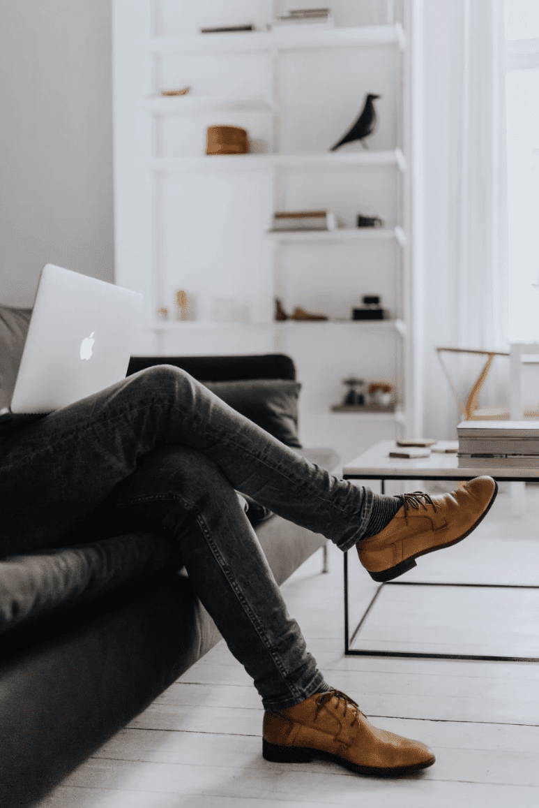 A professional working on a laptop while sitting on a modern sofa, illustrating a tech founder in the Research Triangle succeeding on paper but experiencing shadow burnout, a pattern treated through virtual therapy intensives across NC, SC, and PA.