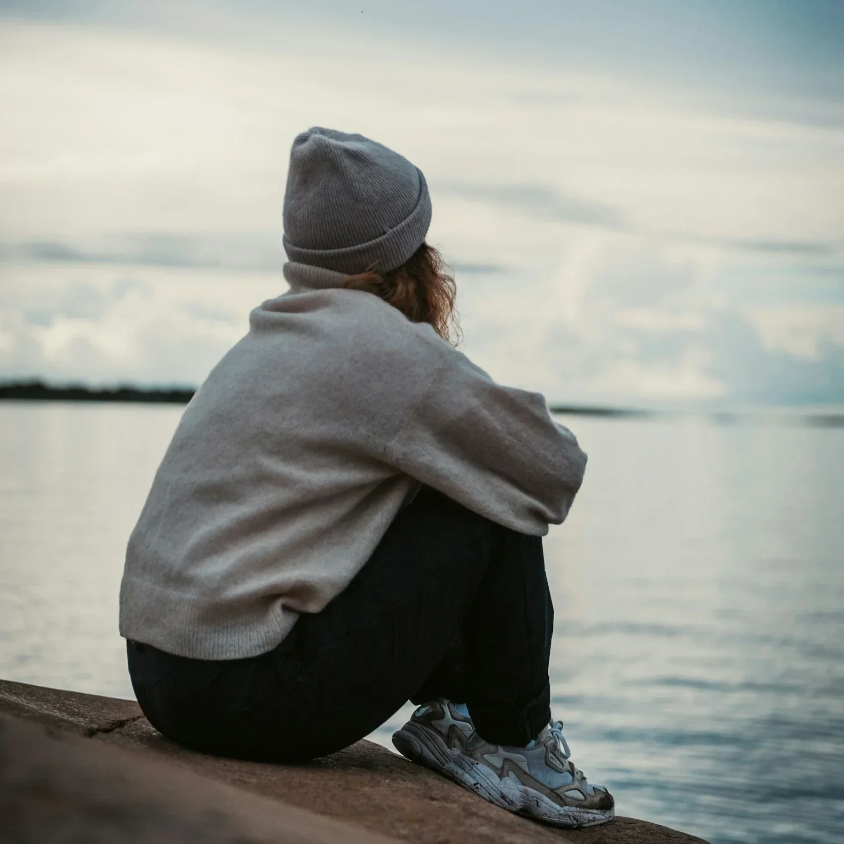 A back view of a person sitting alone by the water, illustrating the isolation often felt when grieving during the holidays, a pattern addressed through trauma therapy in Raleigh, NC