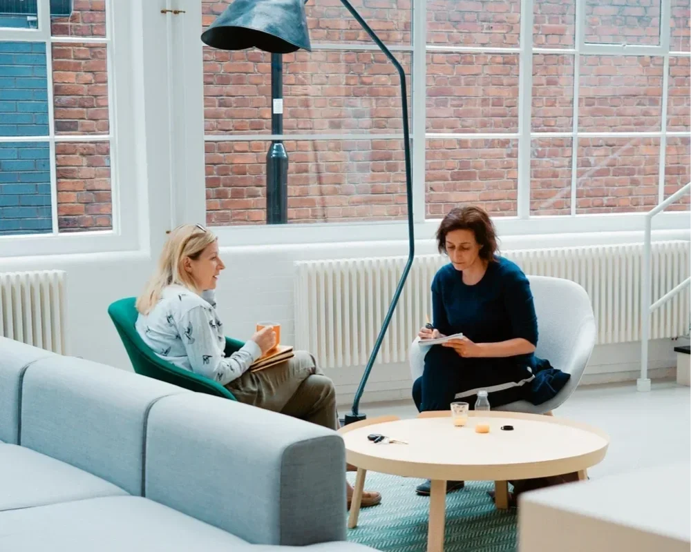 Two women engaging in a deep conversation in a bright, modern office space, representing an in-person trauma therapy intensive session with therapist Mariah J. Zur.