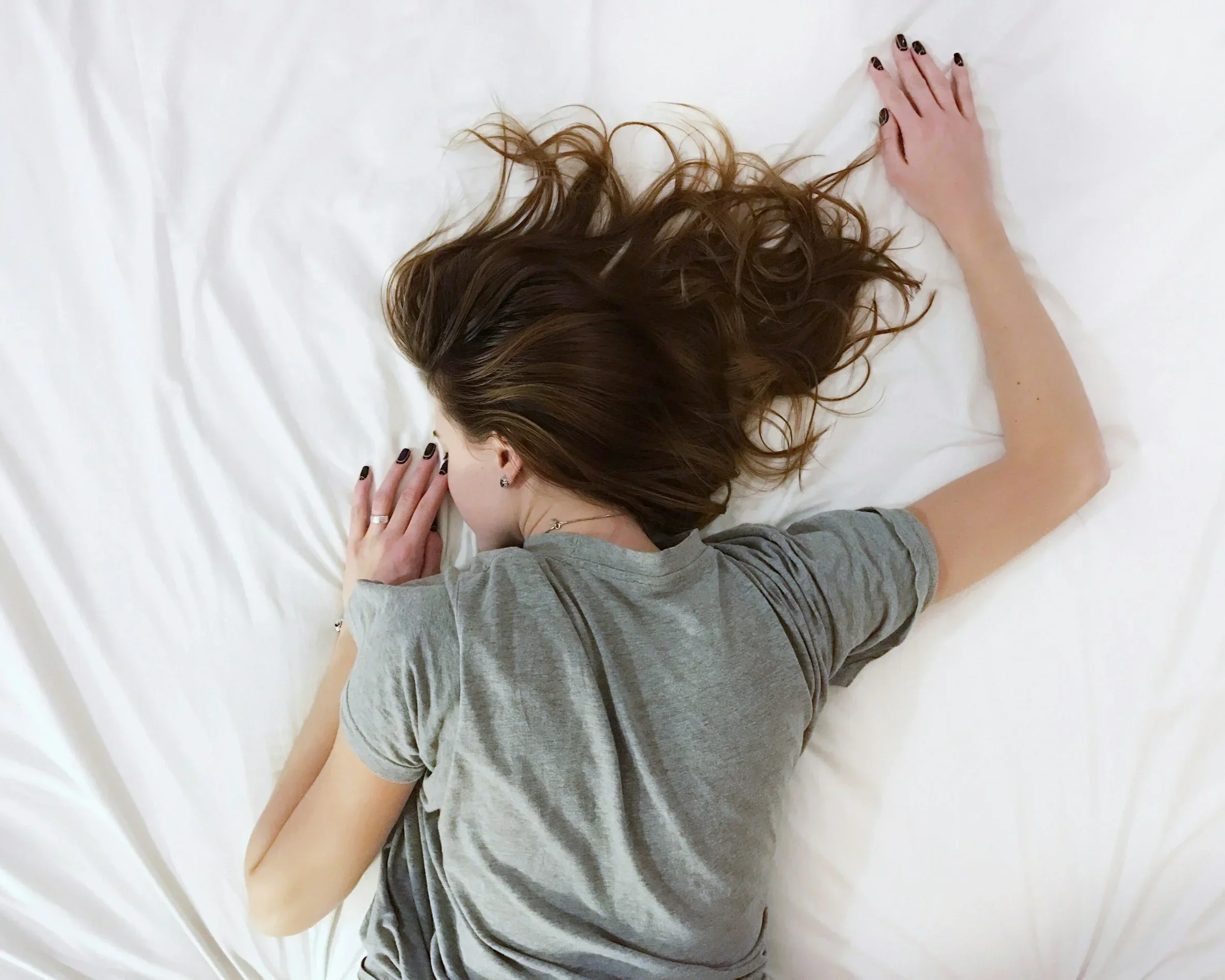 A woman lying face down on a white bed, appearing exhausted and overwhelmed. PA trauma therapist Mariah Zur helps clients recover from the profound emotional burnout and exhaustion caused by toxic relationships and trauma bonds.