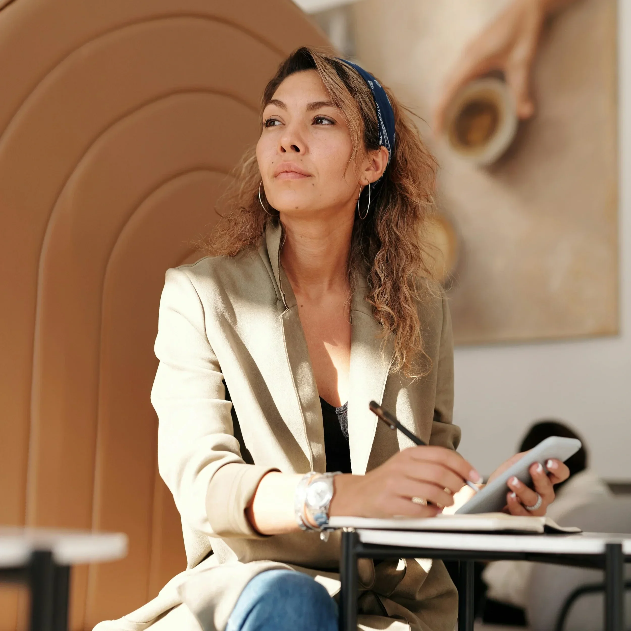 A woman sitting in a sunlit space holding a pen and notebook, looking off thoughtfully. PA trauma therapist Mariah Zur helps high-achievers stop overthinking and process their emotions through mindfulness and therapy.