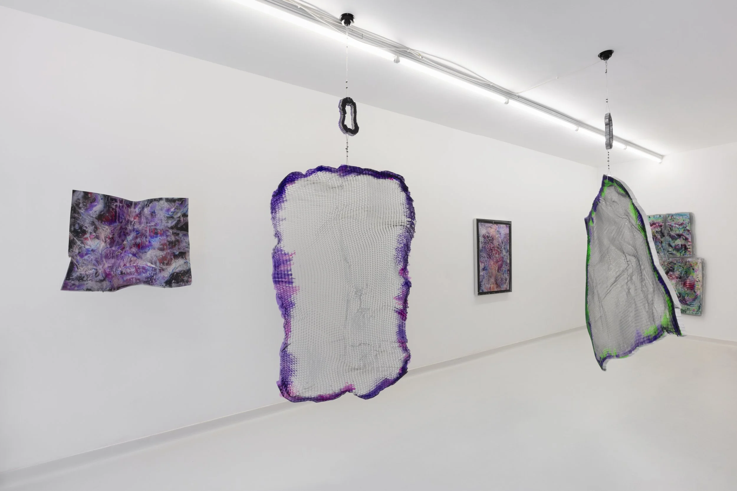 Contemporary art gallery with abstract mixed-media hanging sculptures and framed abstract paintings on white walls.