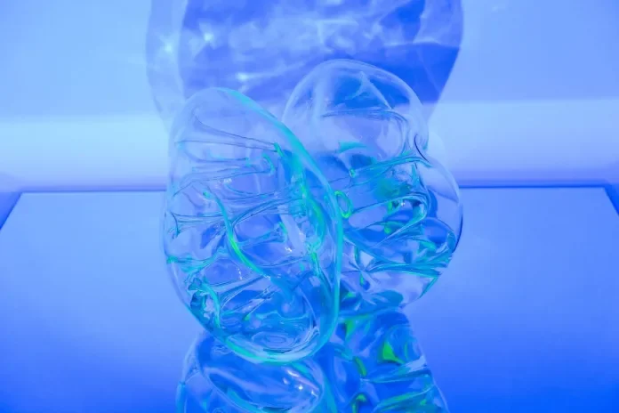 A transparent sculpture of a human brain with neon green and blue lighting effects, displayed on a reflective surface.