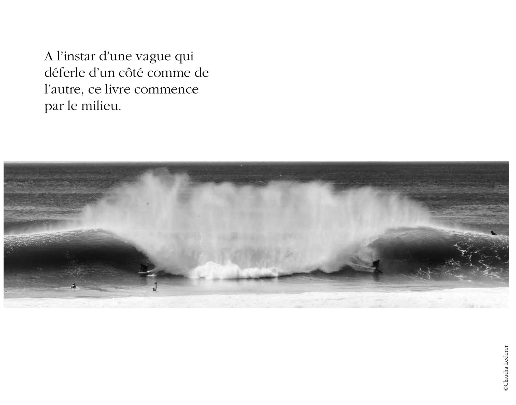 Black and white photo of surfers riding a large wave at the beach, with some surfers in the water and one on the wave.