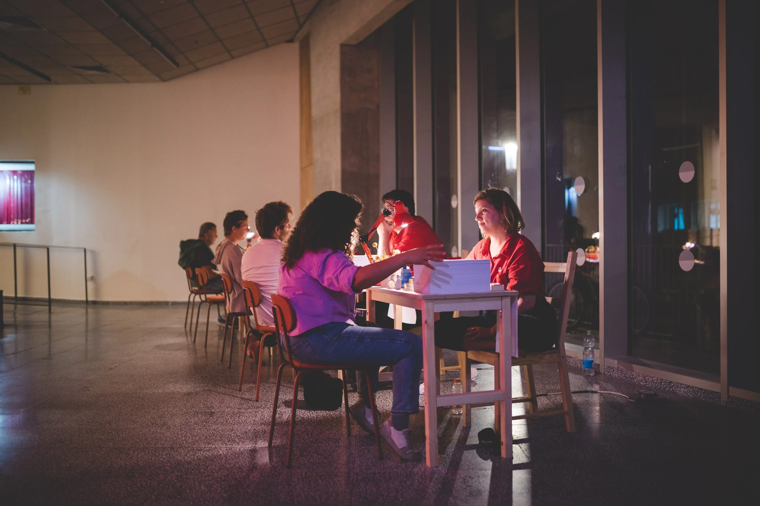 Group of people sitting at tables in a dimly lit indoor space, engaging in conversation.