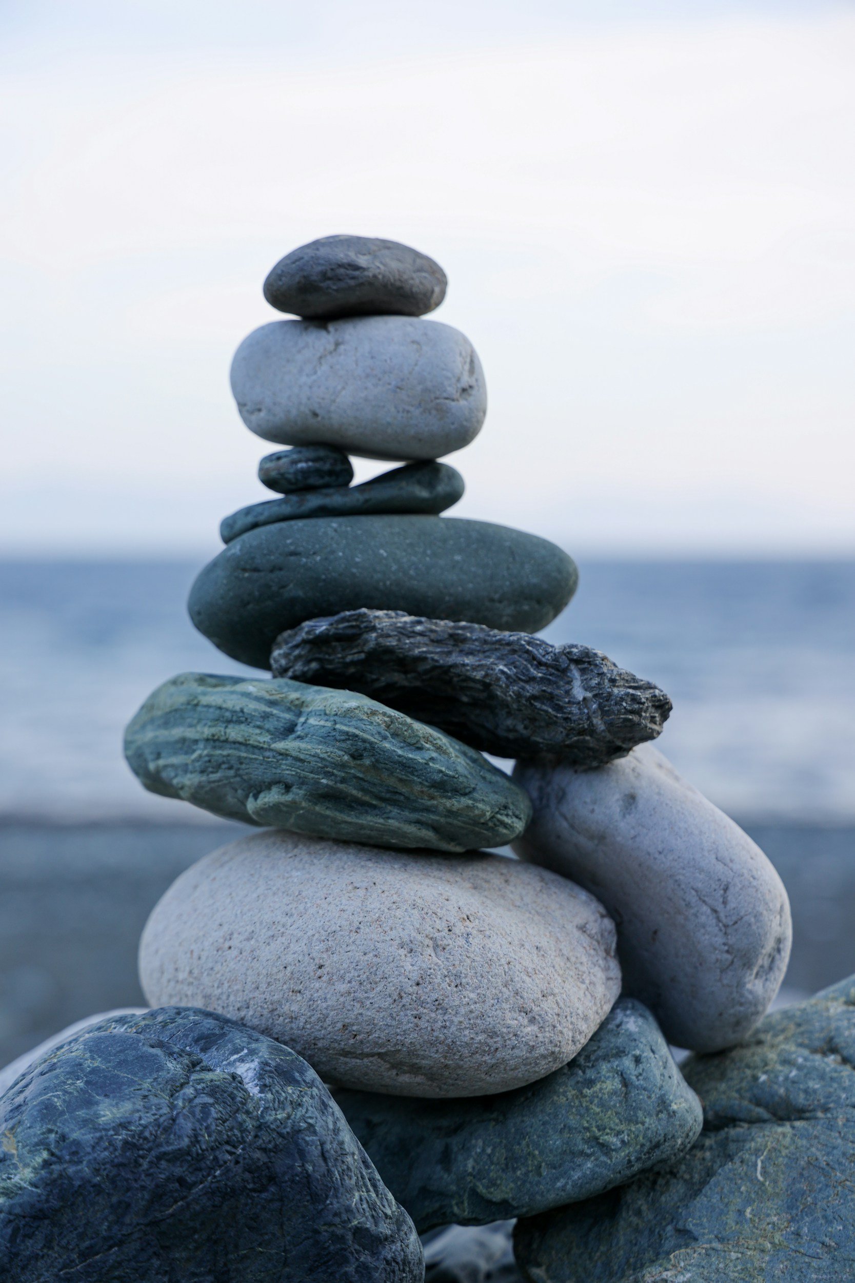 Stack of smooth, rounded stones balanced on each other against a cloudy sky and ocean background.