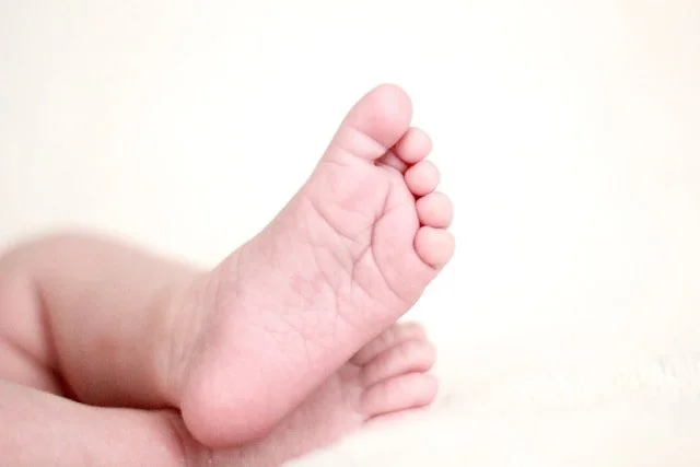 Close-up of a baby's foot with toes curled, resting on a soft, light-colored surface.