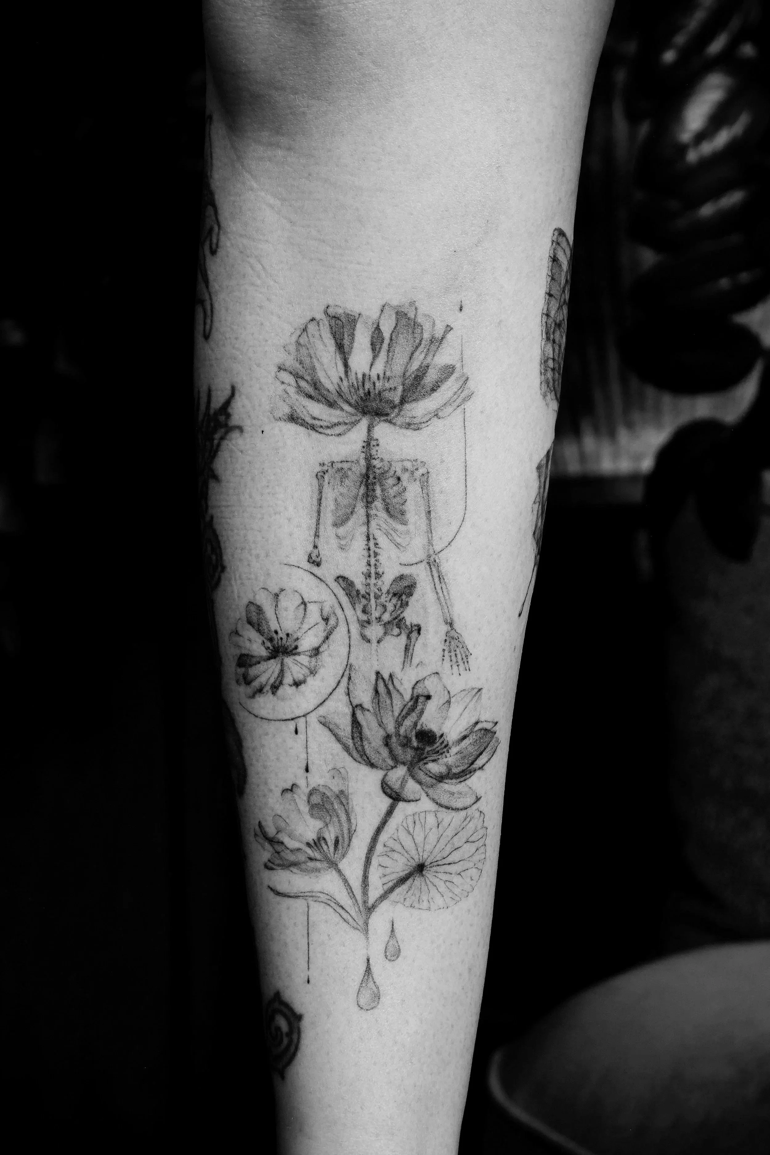 Close-up of a person's arm with x-ray custom tattoos done by Ola Getka, including a large flower, a skeleton, and abstract designs, in black and white.