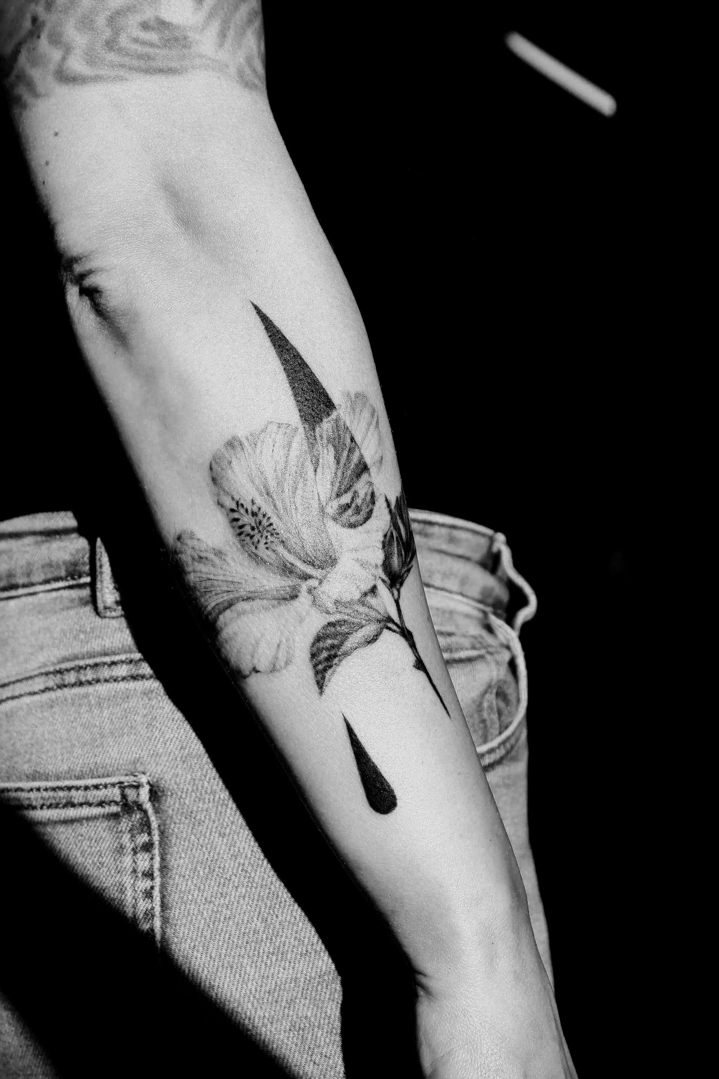 Close-up of a person's arm with a floral tattoo customized and done by Ola Getka in Aura Tattoo Reykjavik, presenting realistic hibiskus flower and geometric additions, in black and white.