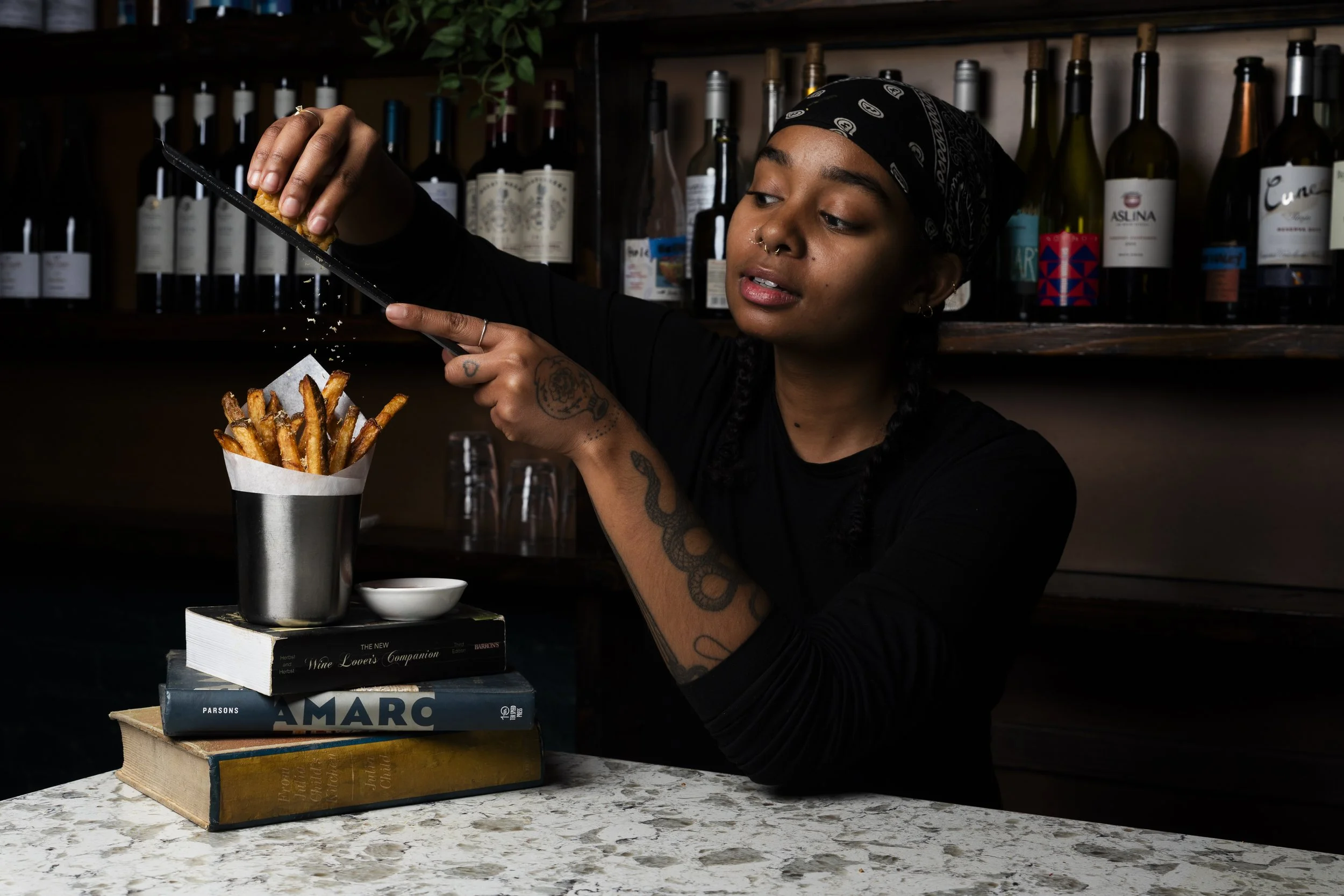 A woman is shaving cheese on a plate of fries stacked on books.